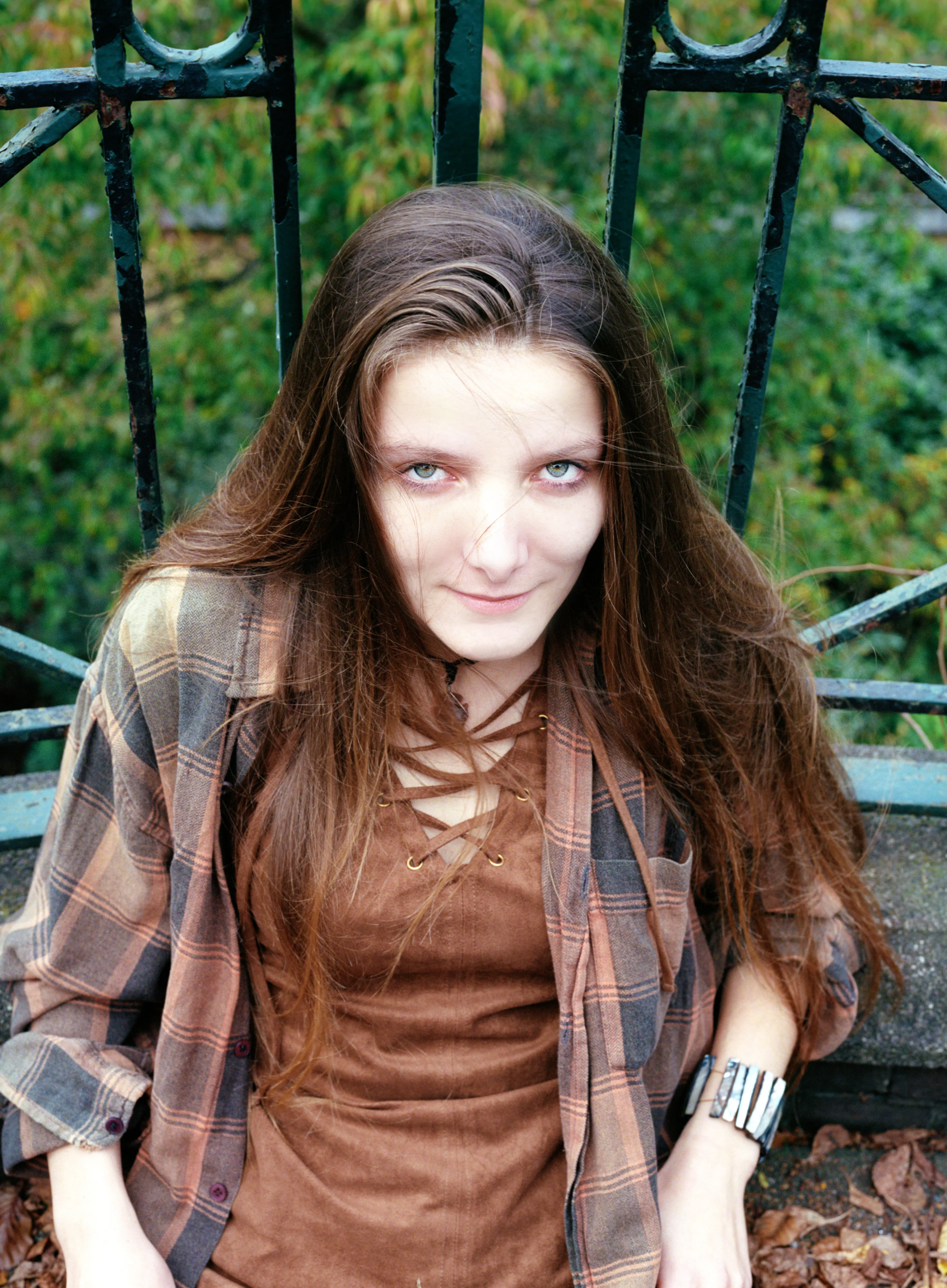 Bella looking up into the camera against a black iron gate and autumn greenery, a direct gaze.