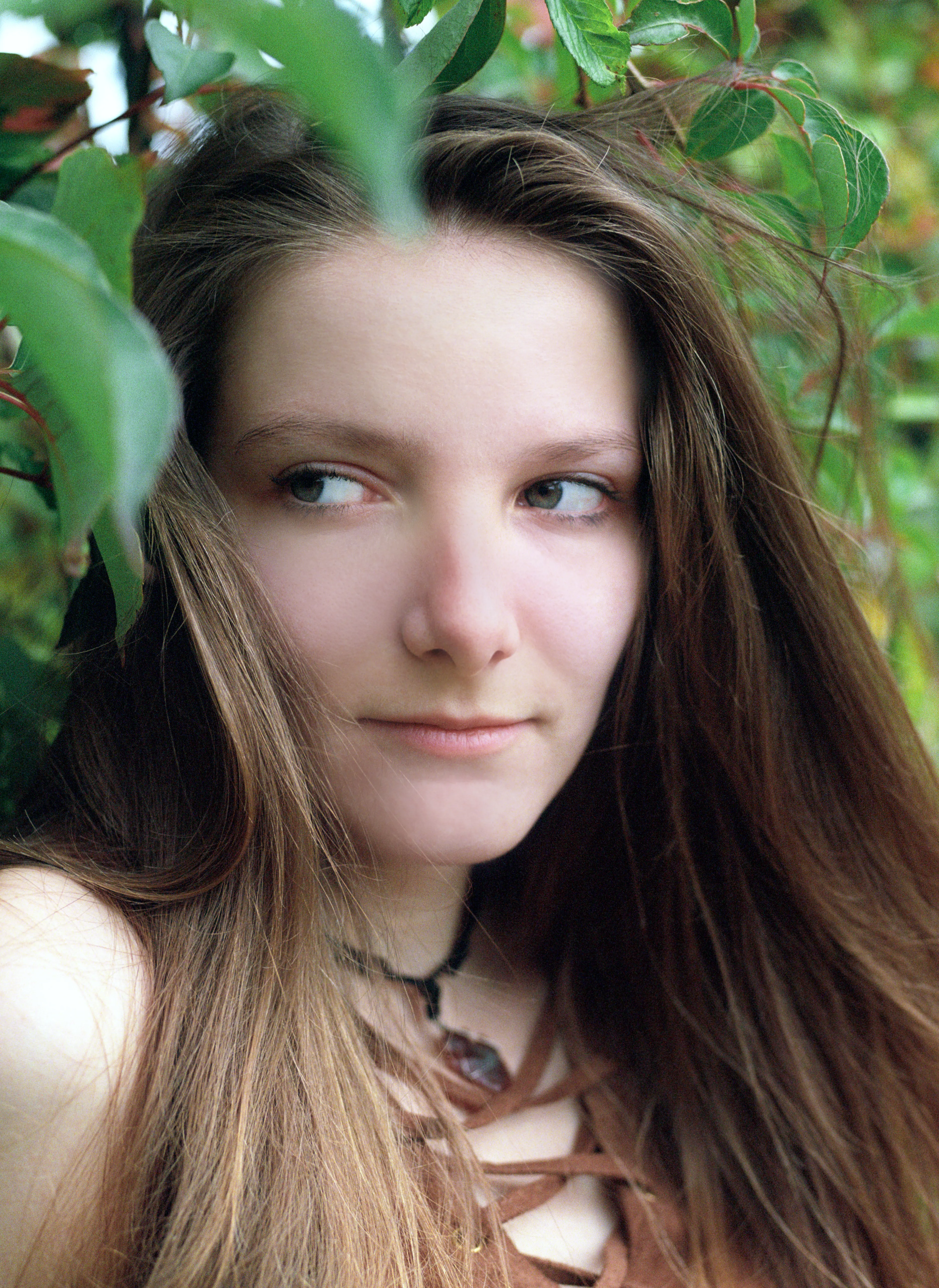 Bella's face among green foliage, eyes cut to the side, a pendant at her throat.