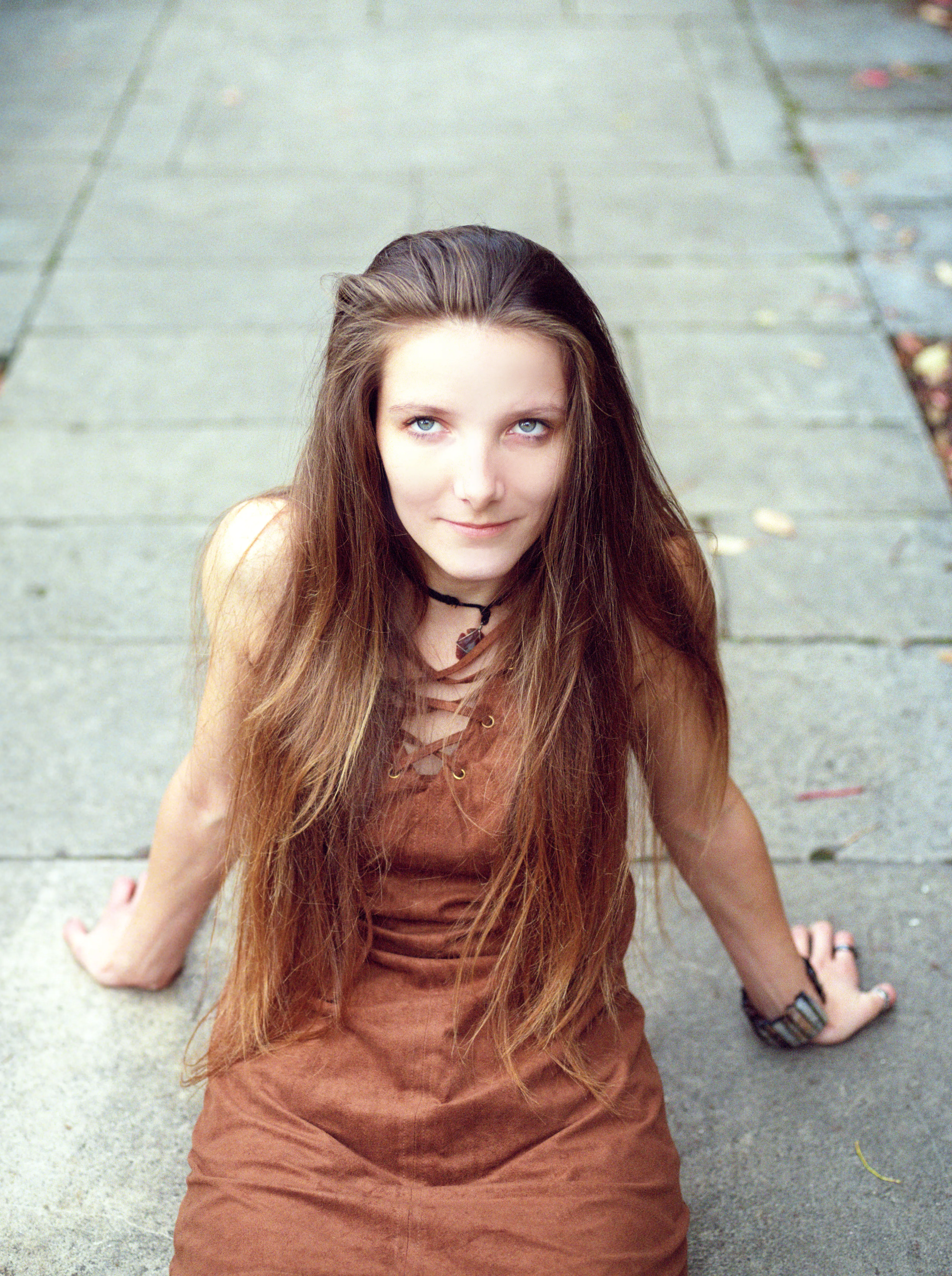 Bella sitting on stone paving scattered with autumn leaves, hands planted behind, looking up at the camera.