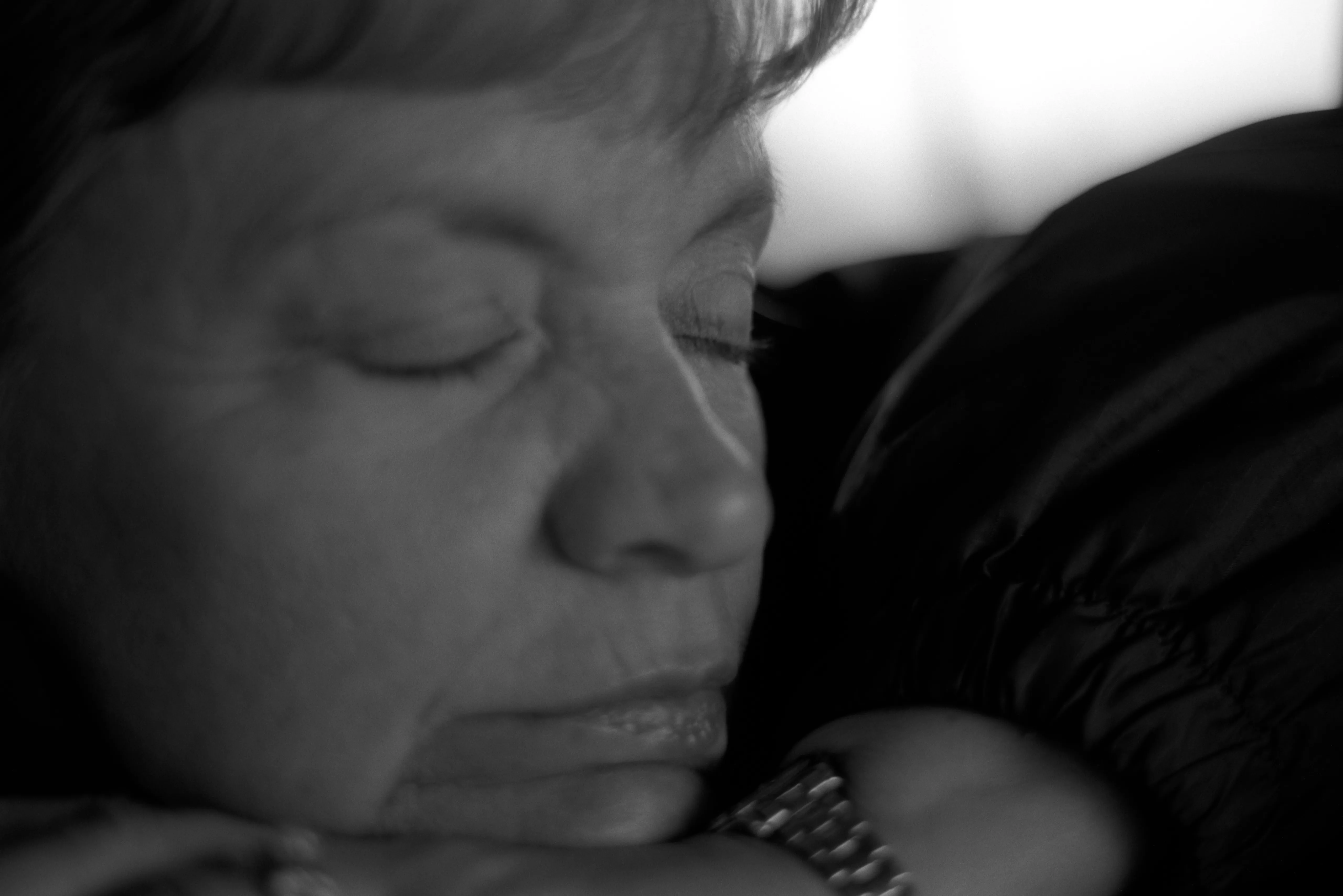 Brenda asleep, her head resting on her forearm, eyes closed, soft light across her face against shadow. Black and white.