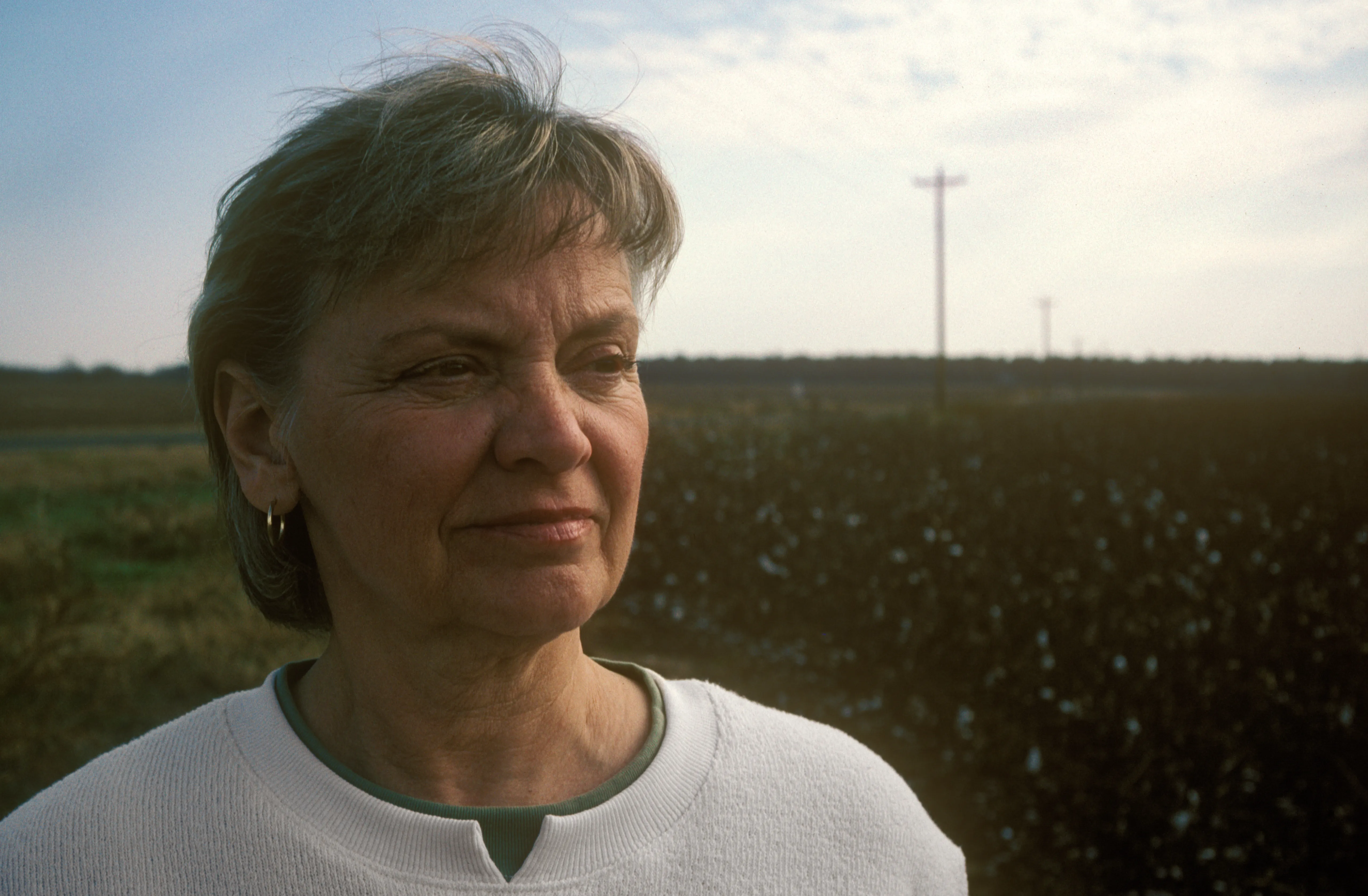 Brenda standing in an open field at sunset, in a white top, looking off to one side, the low sun warming her face.