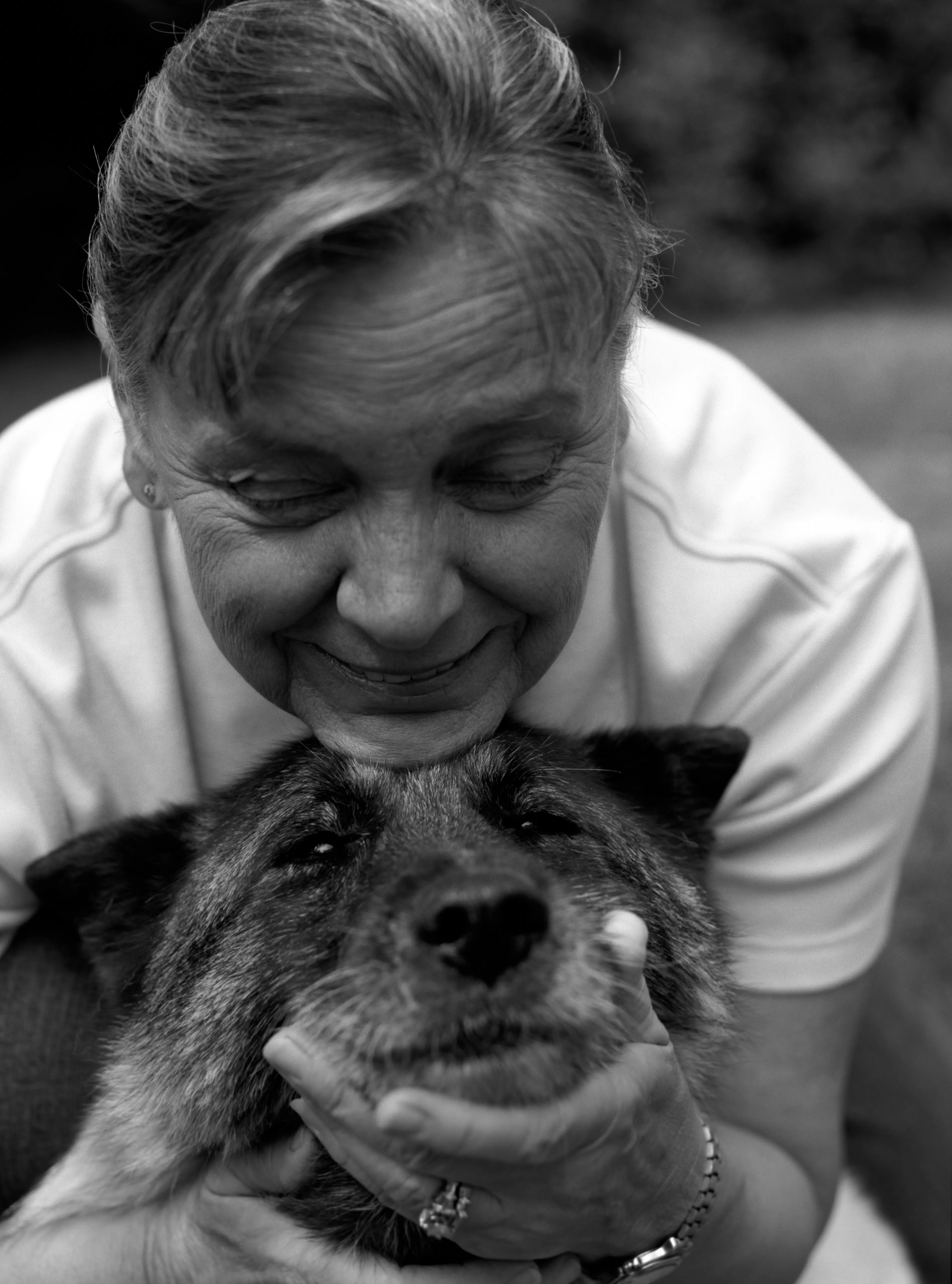 Brenda cupping Marilla's muzzle in one hand, her face above the dog, eyes nearly closed. Black and white.