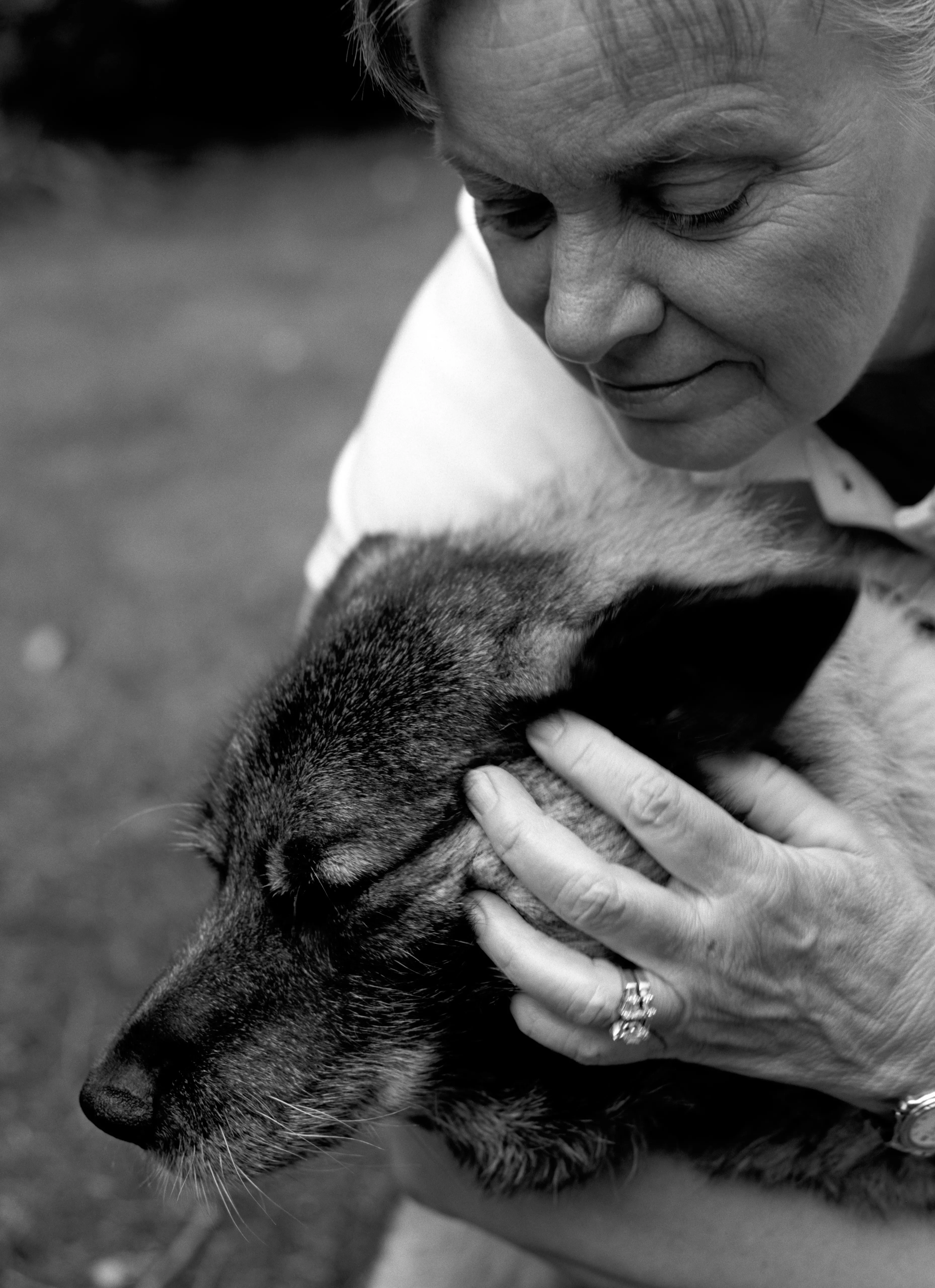 Brenda in profile, her face lowered over Marilla, eyes closed, one hand resting on the dog's chest. Black and white.
