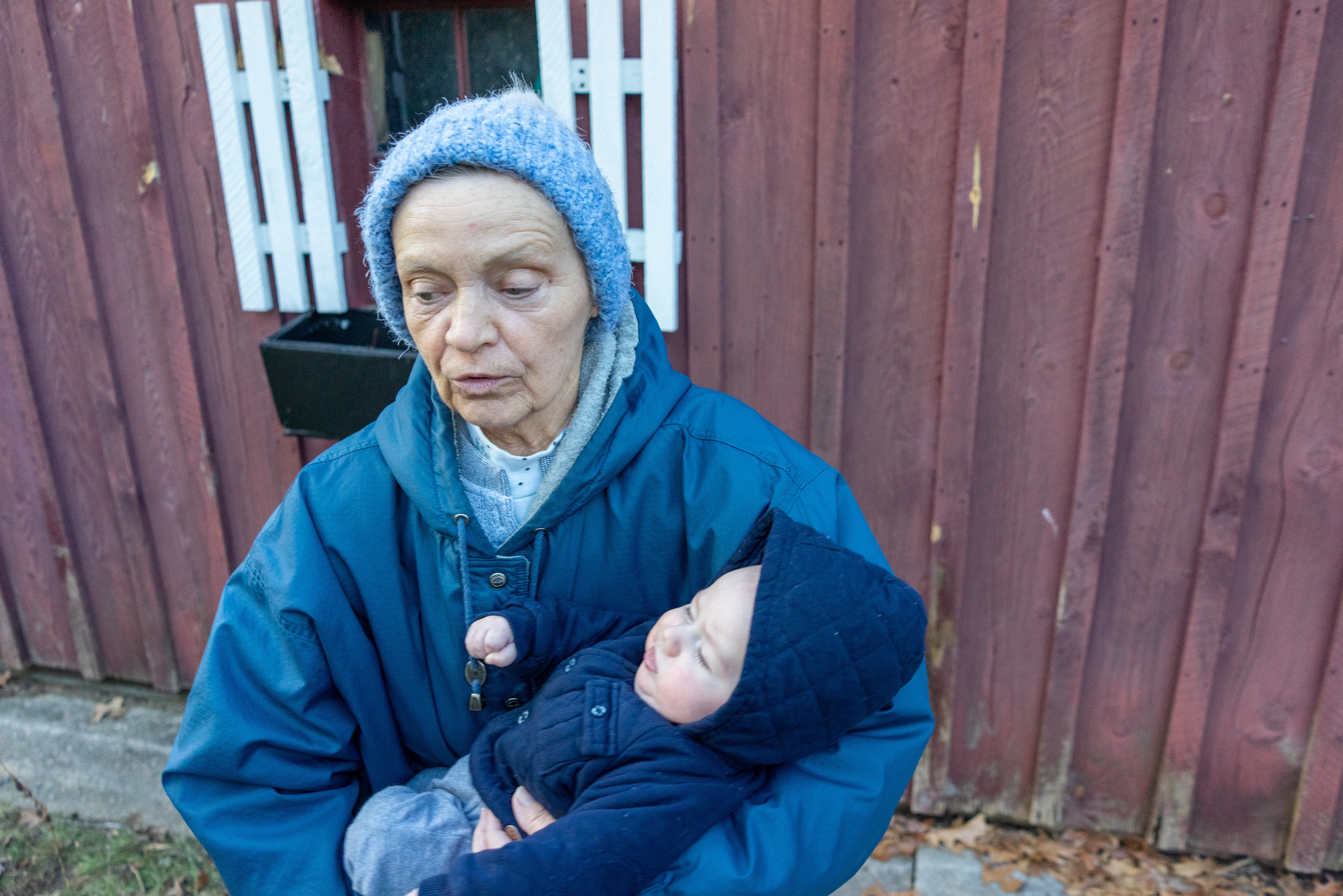 Brenda in the same hat and coat holding her sleeping grandson, her eyes lowered to the child.