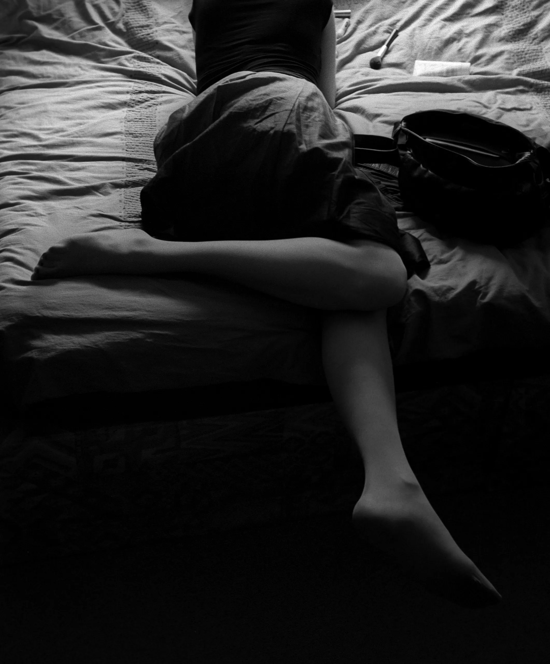 A figure lying on a bed, legs crossed, the lower frame falling into shadow.