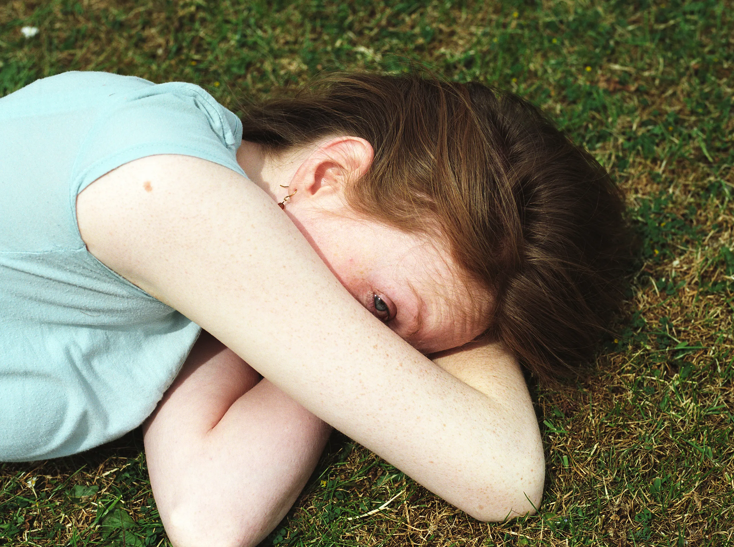 Catherine lying on grass, one eye watching over her crossed arms.