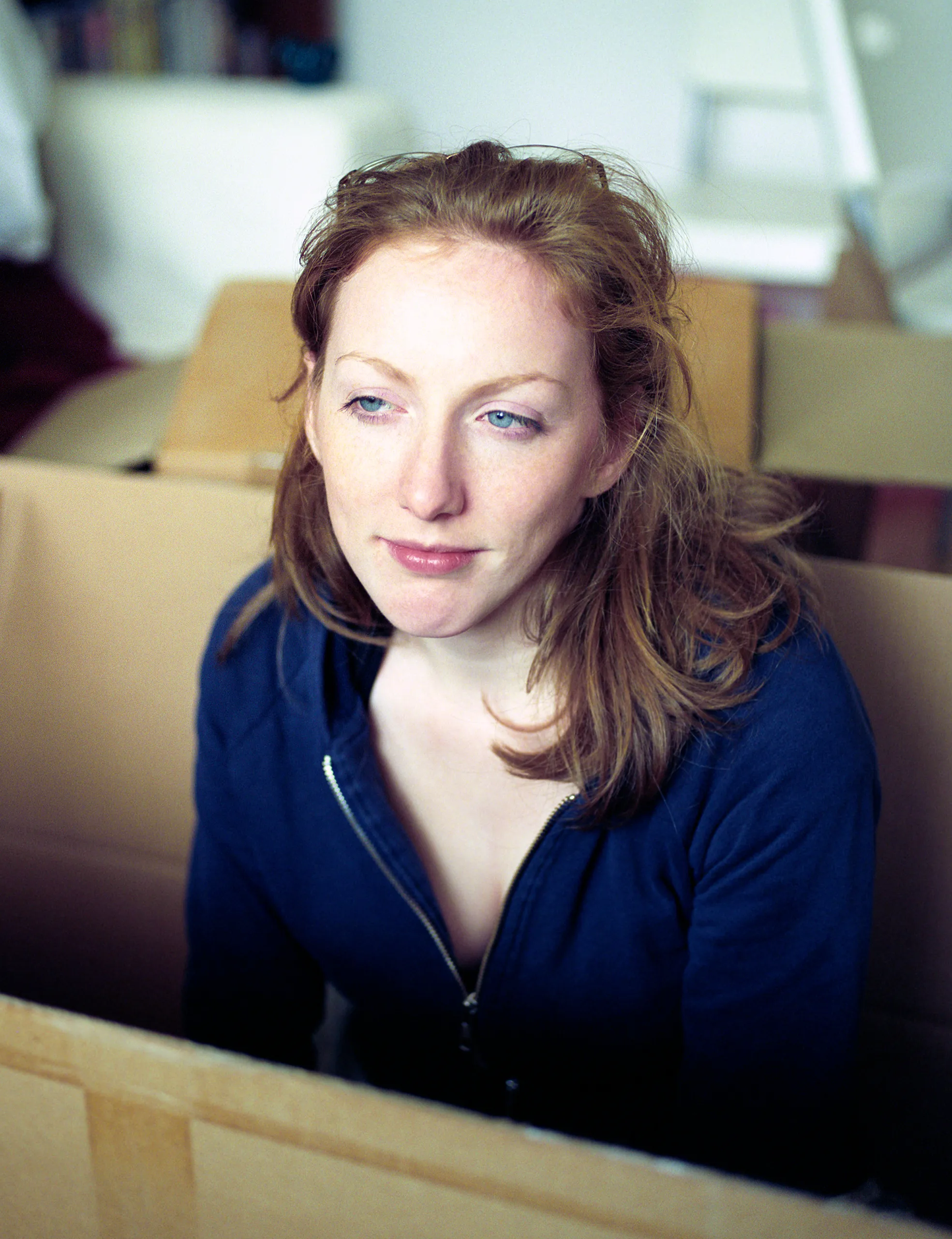 Catherine among cardboard boxes, looking to camera.