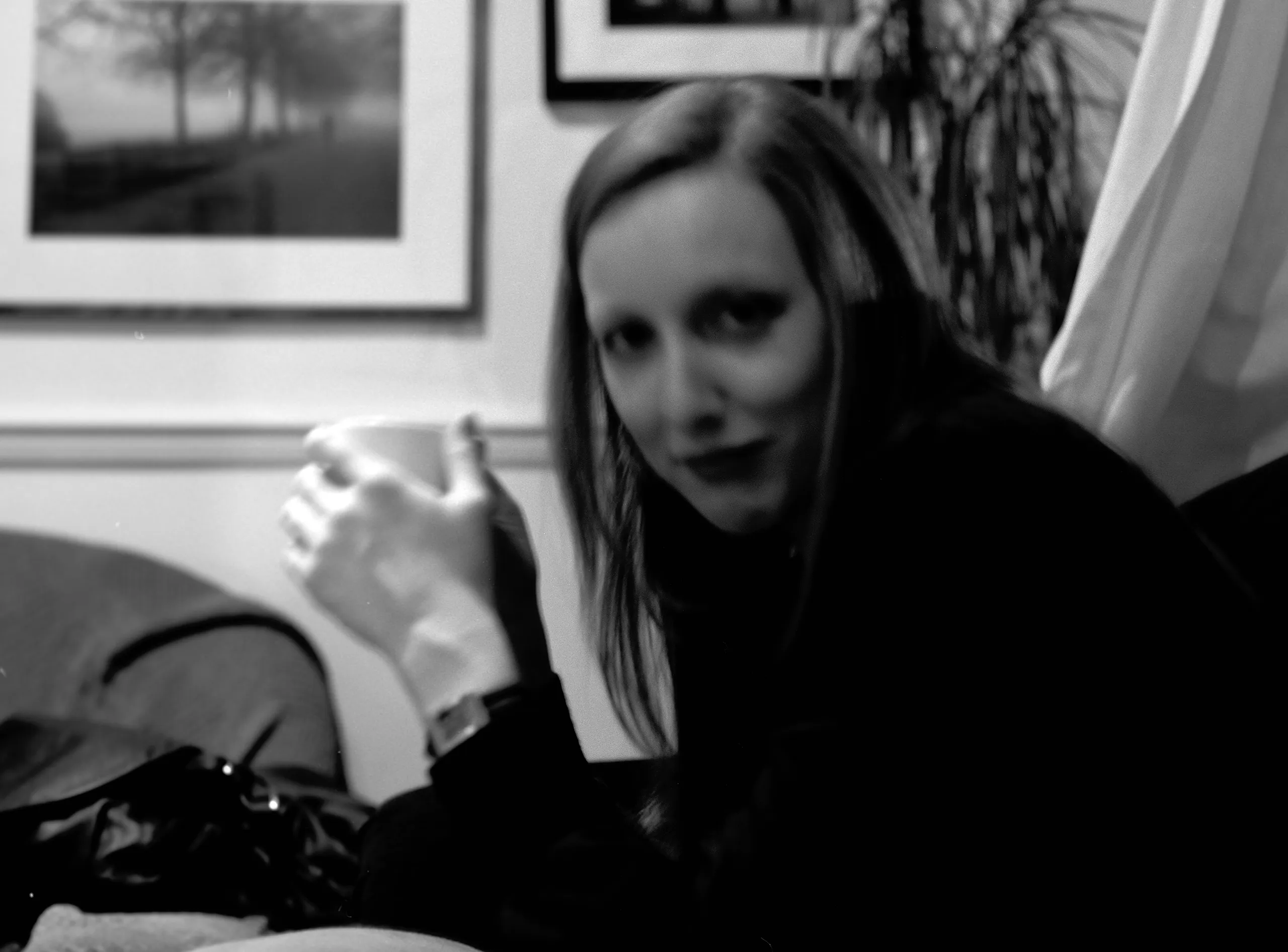 Catherine holding a mug in a dim sitting room, a framed photograph behind her.