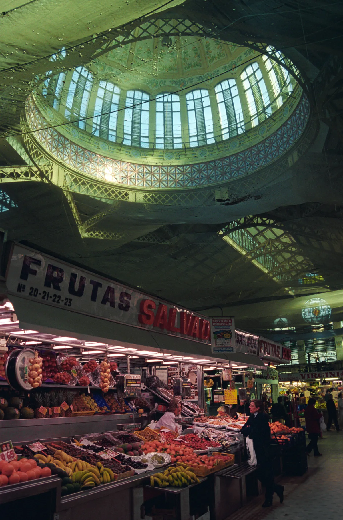 Two women talking across heaped fruit at a market stall, the painted dome above.