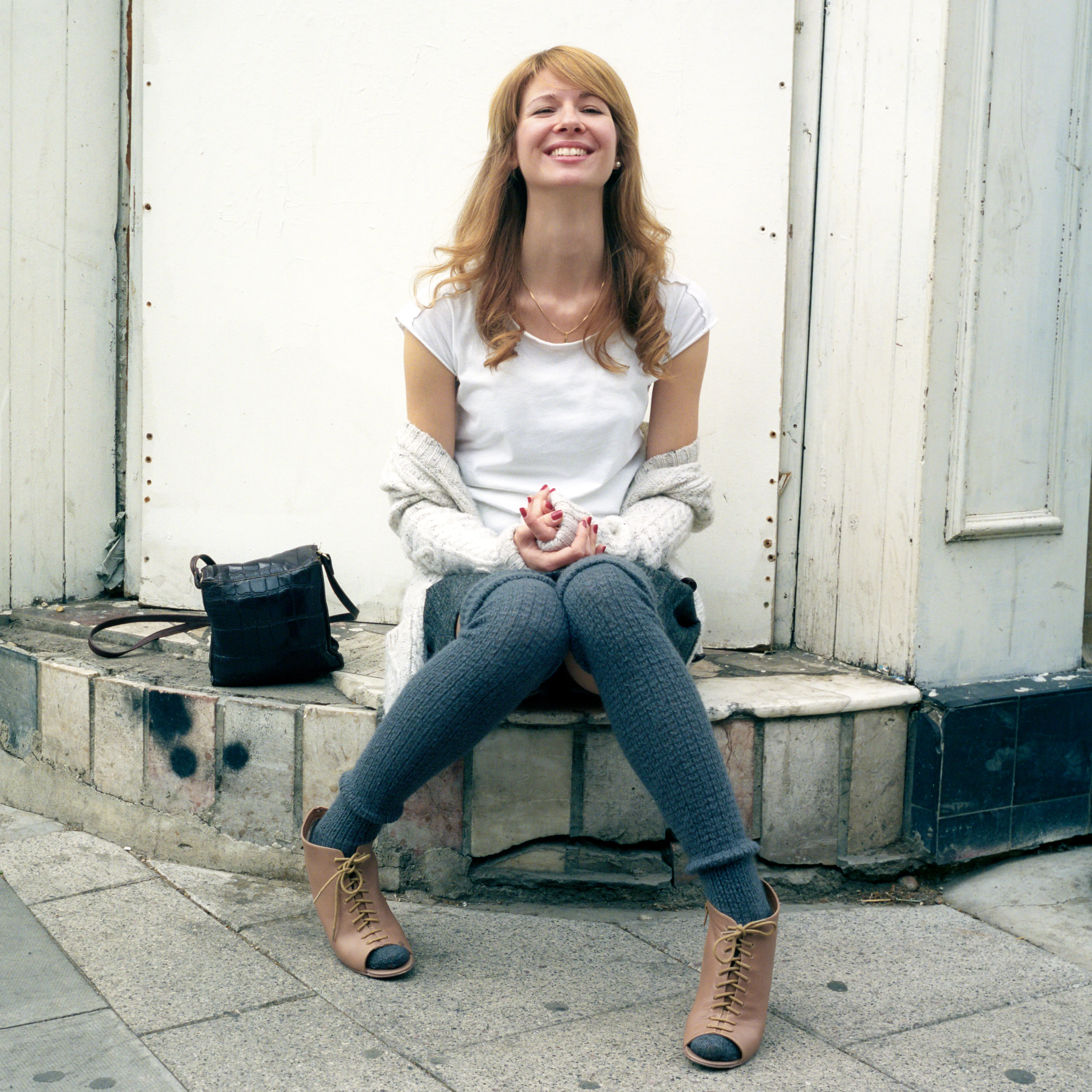 Eva seated on a doorstep, laughing, her hands clasped together over her knees.
