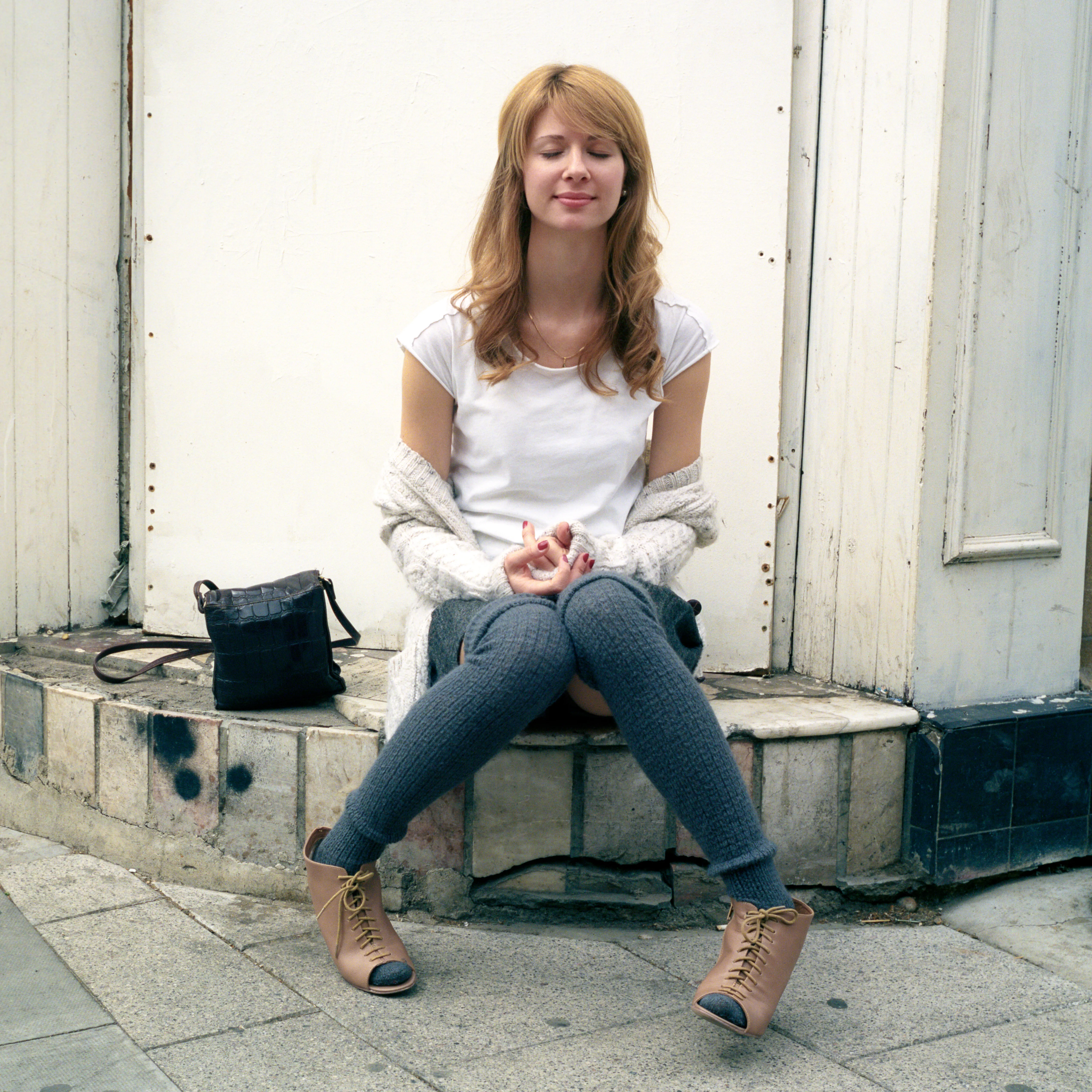 Eva seated on a doorstep, eyes closed, hands resting together in a meditative gesture.