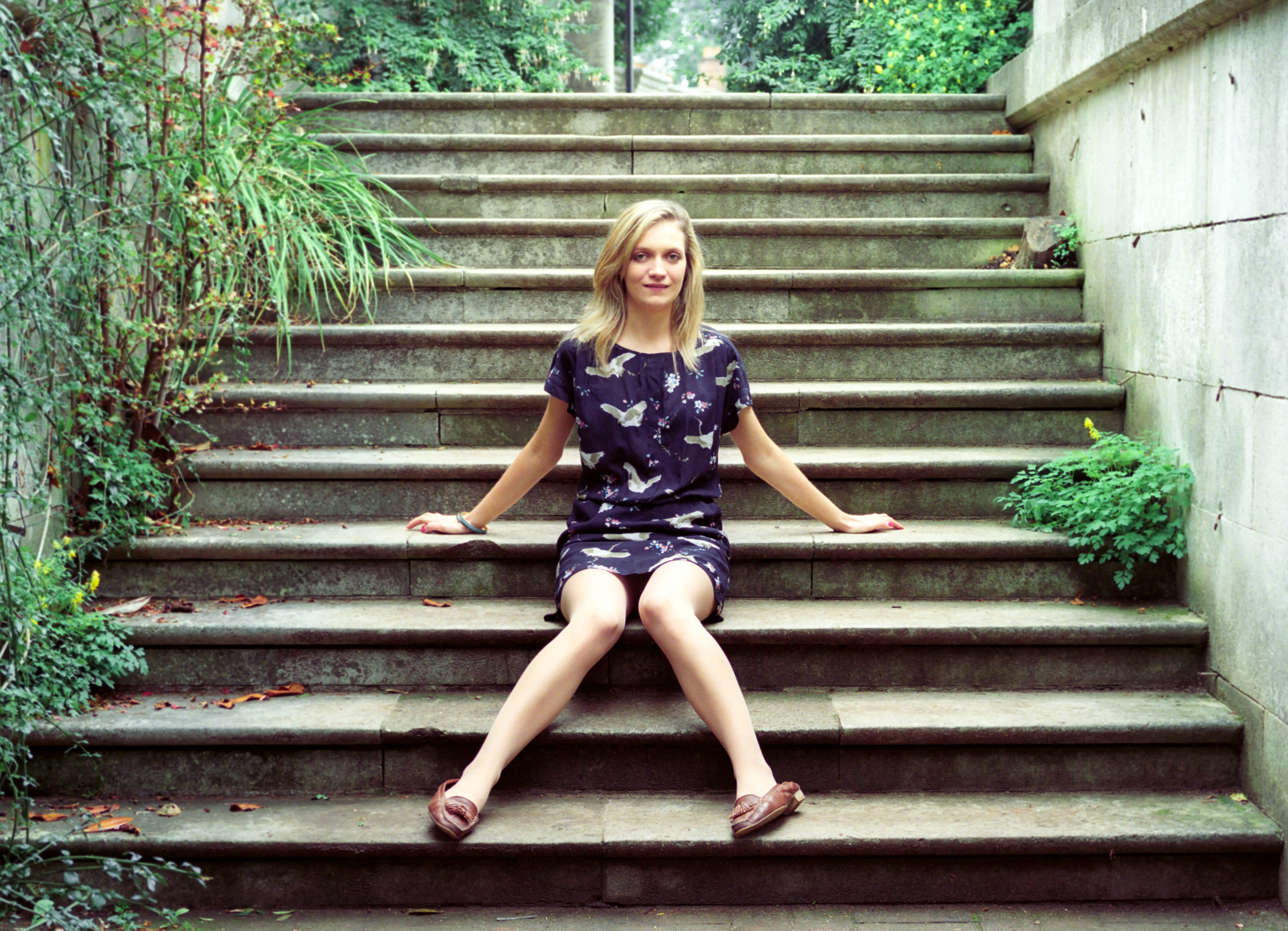 Hannah seated on a broad flight of stone steps, arms braced, looking at the camera.