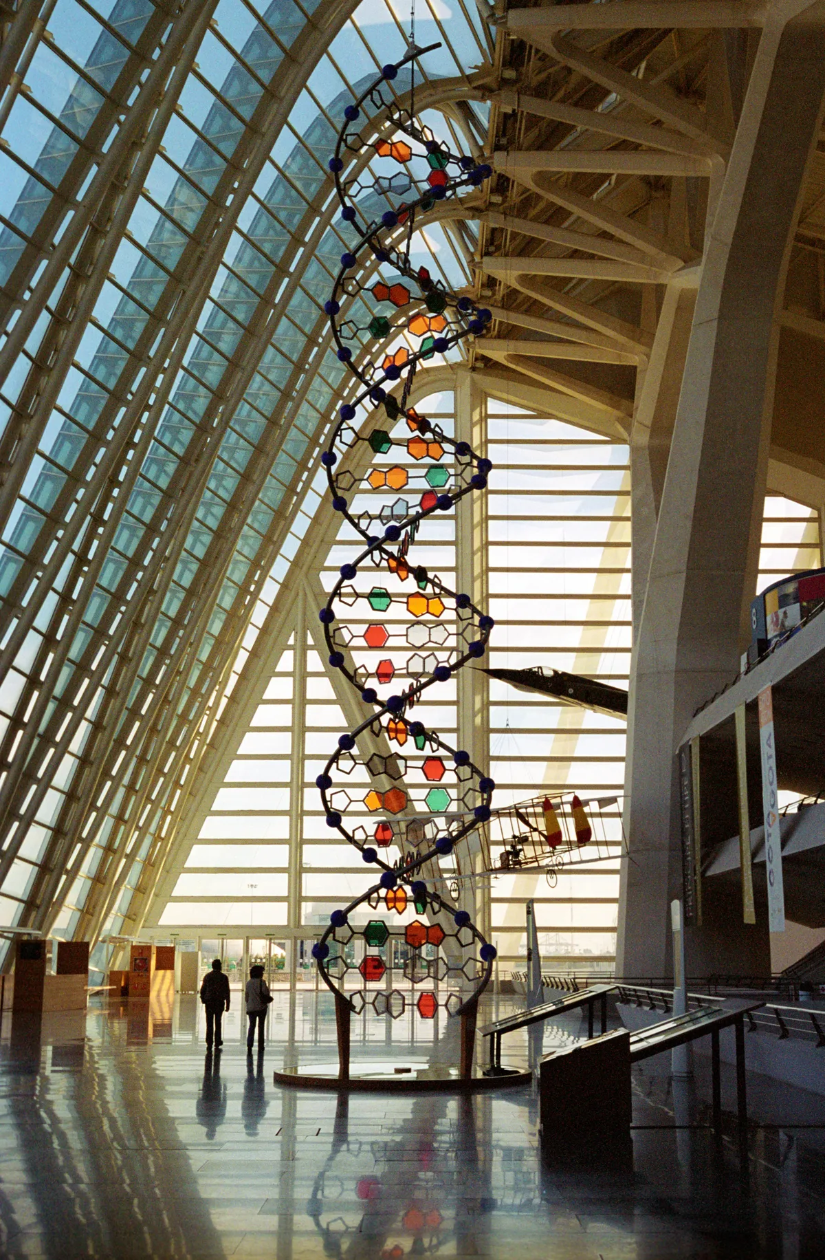 The DNA sculpture close to — coloured hexagons threaded on the black double helix against the glass wall.