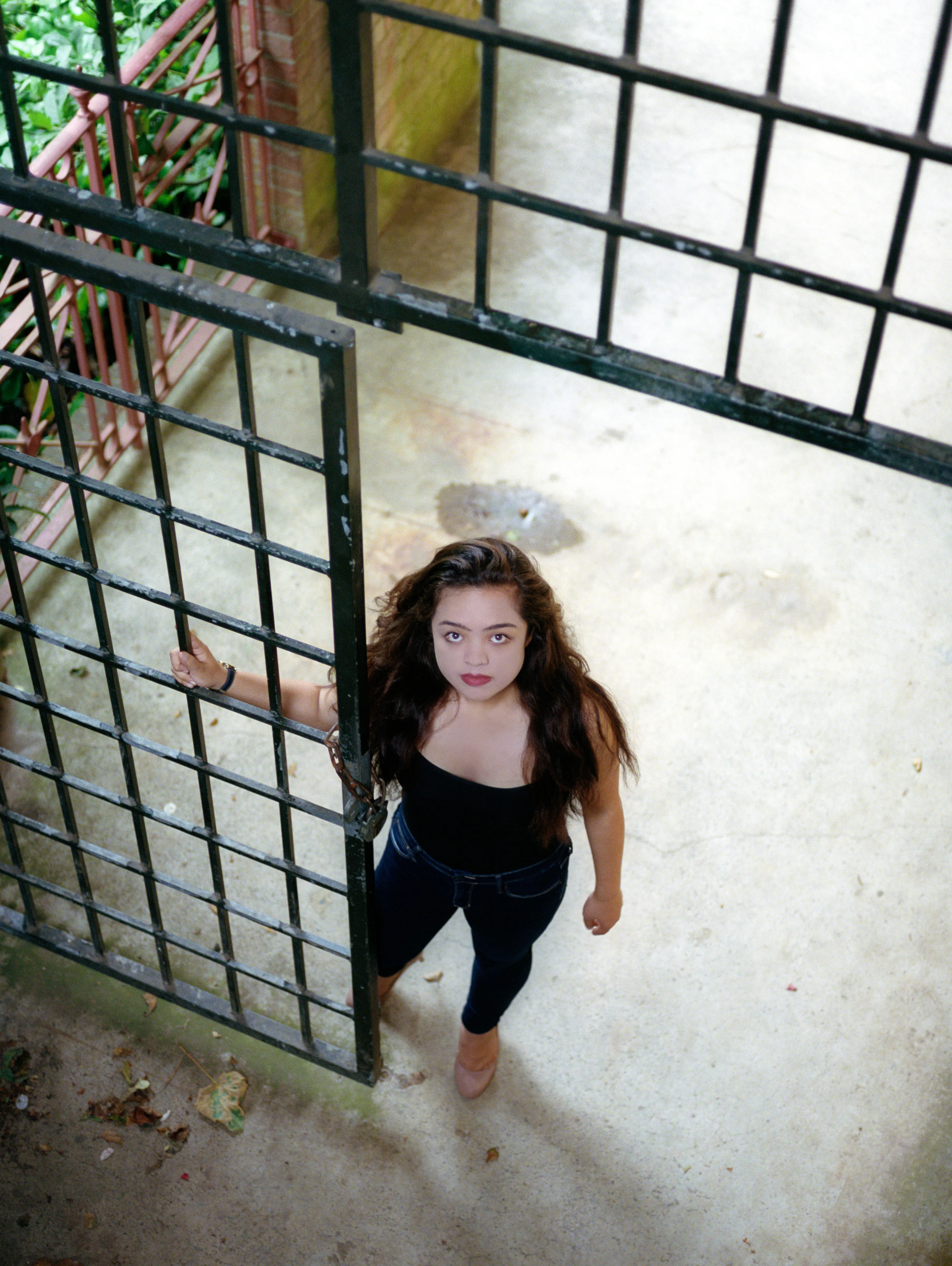 Seen from above, Kiana stands beside an open metal gate, one hand on the bars, looking up towards the camera.