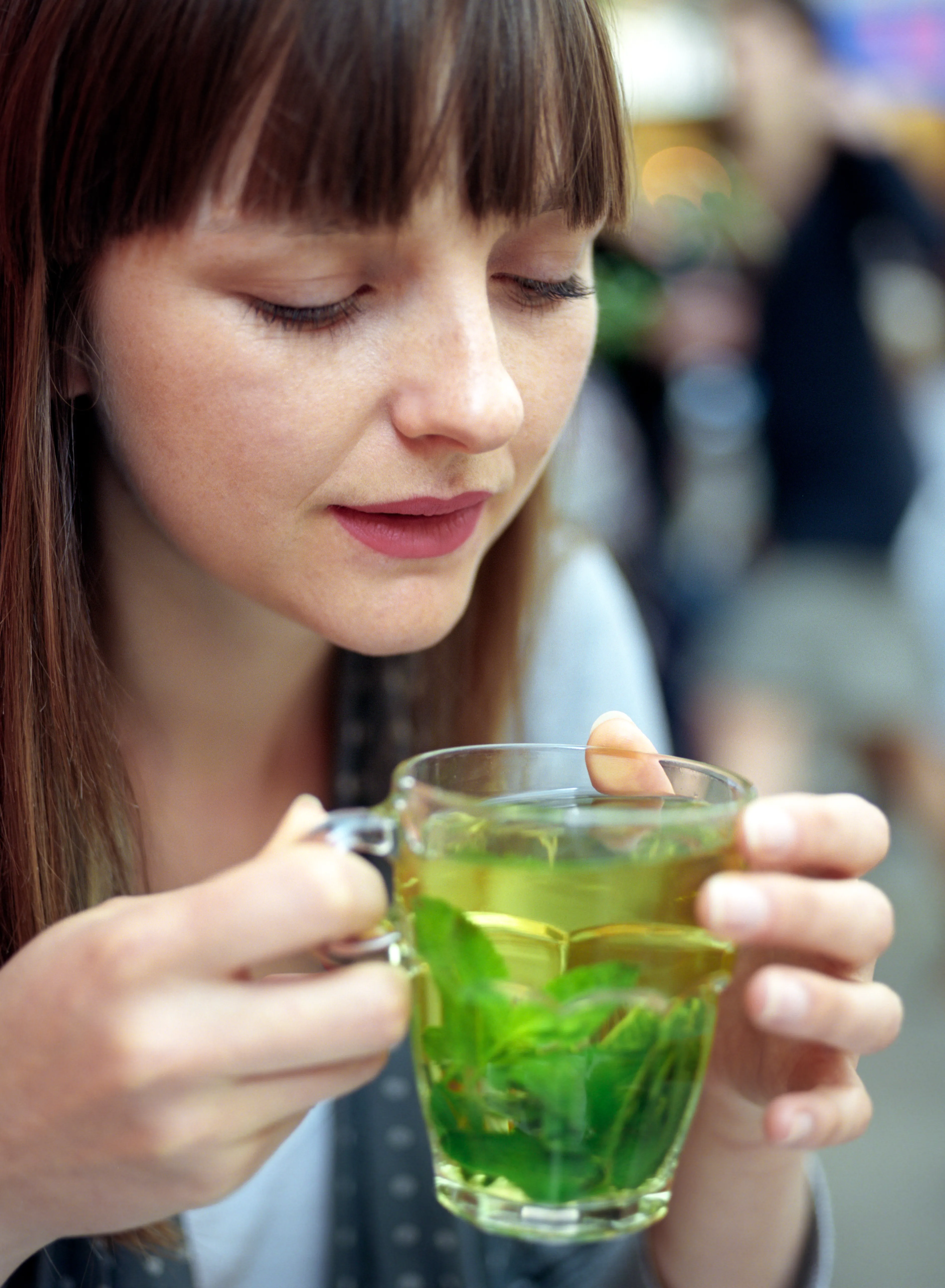 Lauren holding a glass cup of mint tea in both hands, looking down at it, at an outdoor cafe.