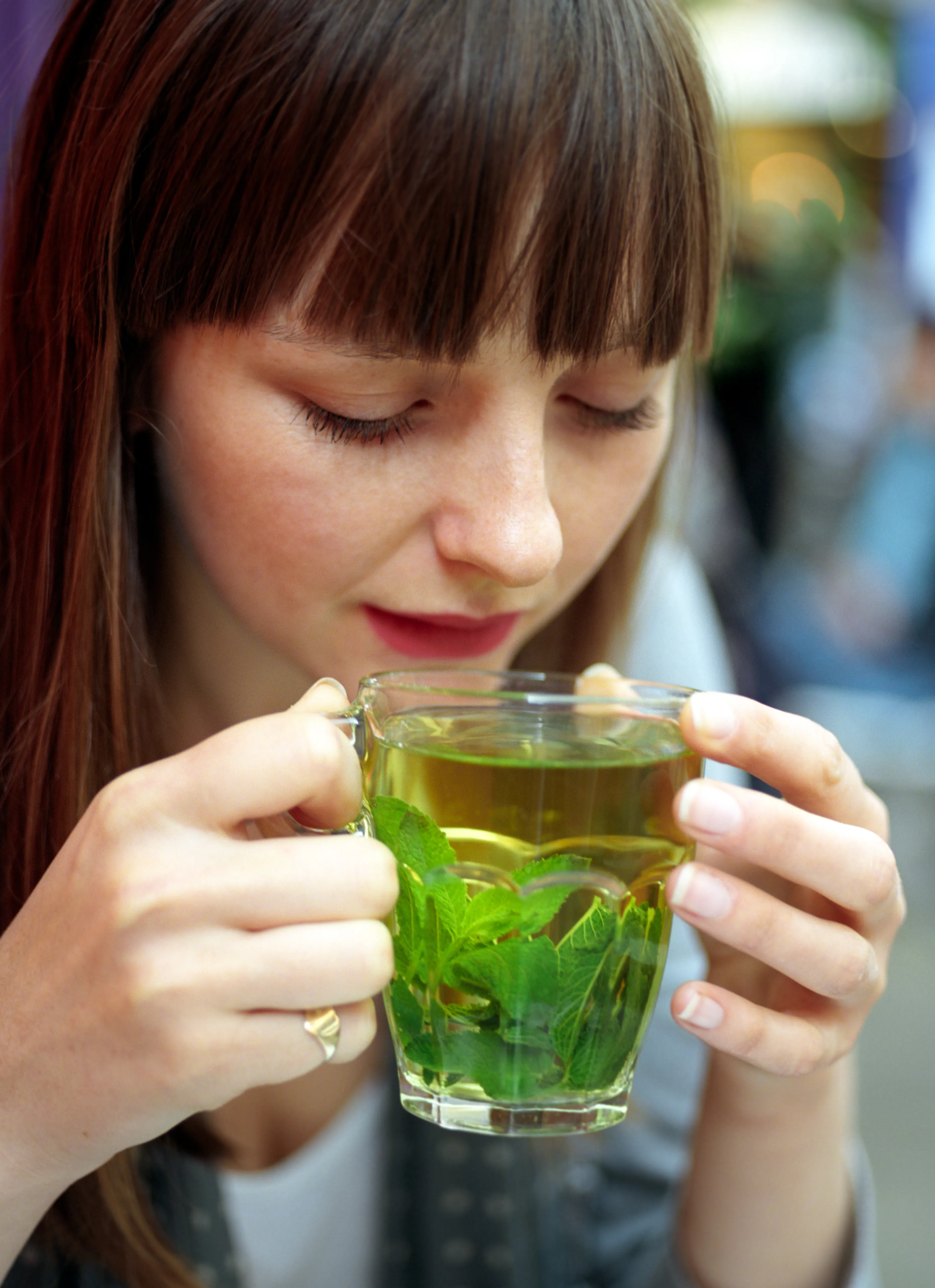 Lauren raising a glass cup of mint tea towards her face, eyes lowered, at an outdoor cafe.