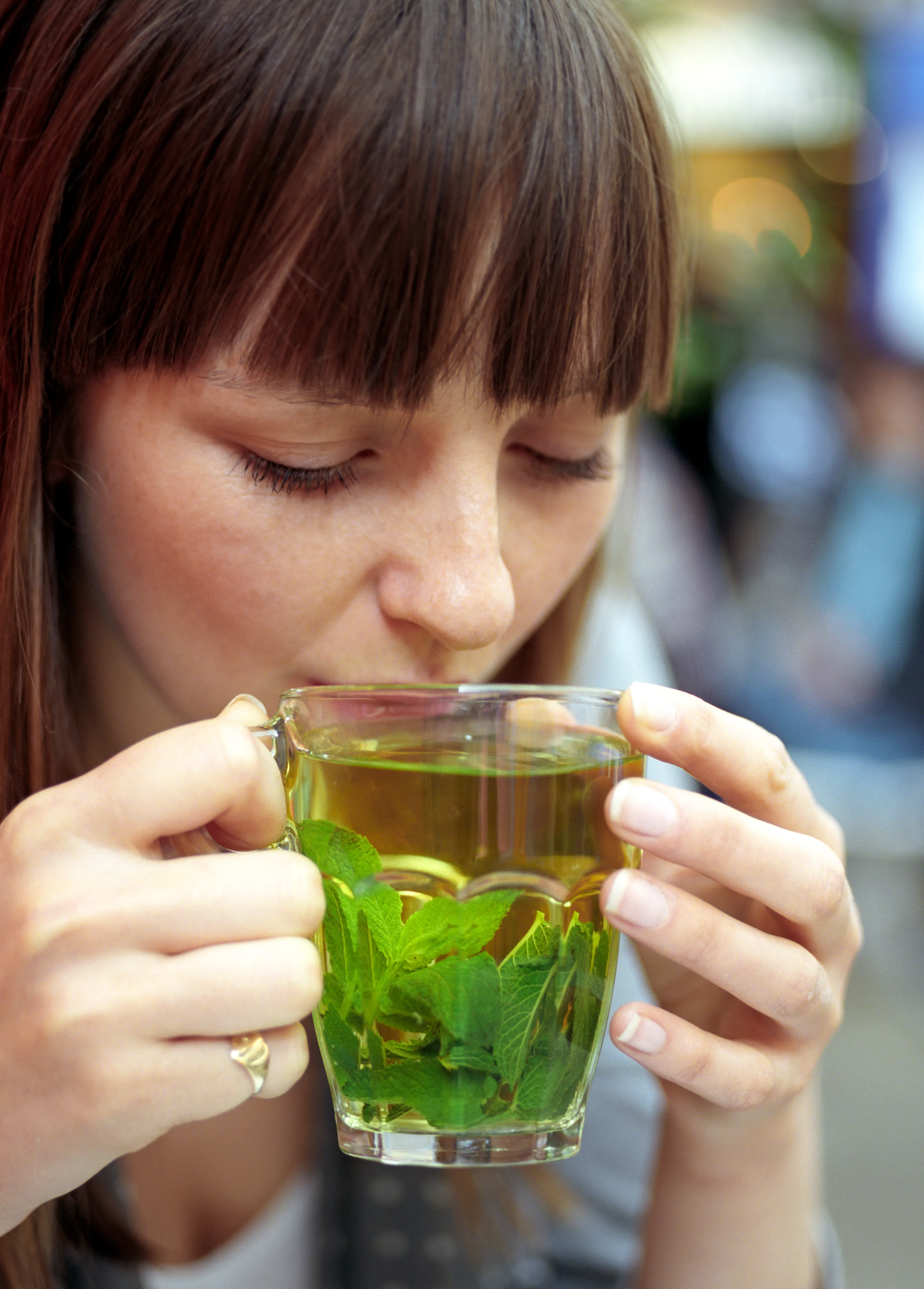 Lauren drinking from a glass cup of mint tea, eyes closed, the cup held in both hands.