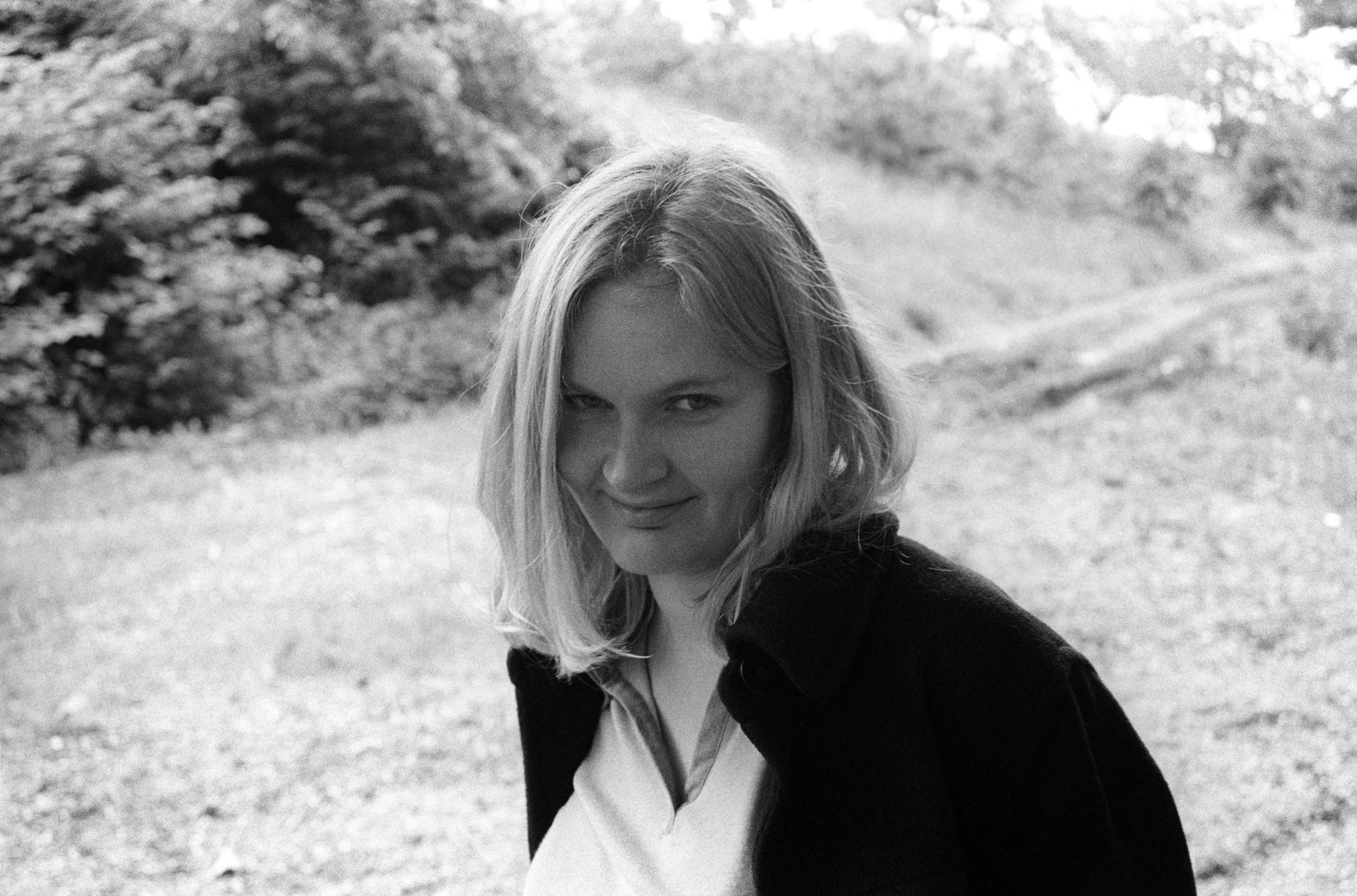 Liddy in three-quarter view on a moor or heath, hair falling across one eye, giving a sly inward smile.