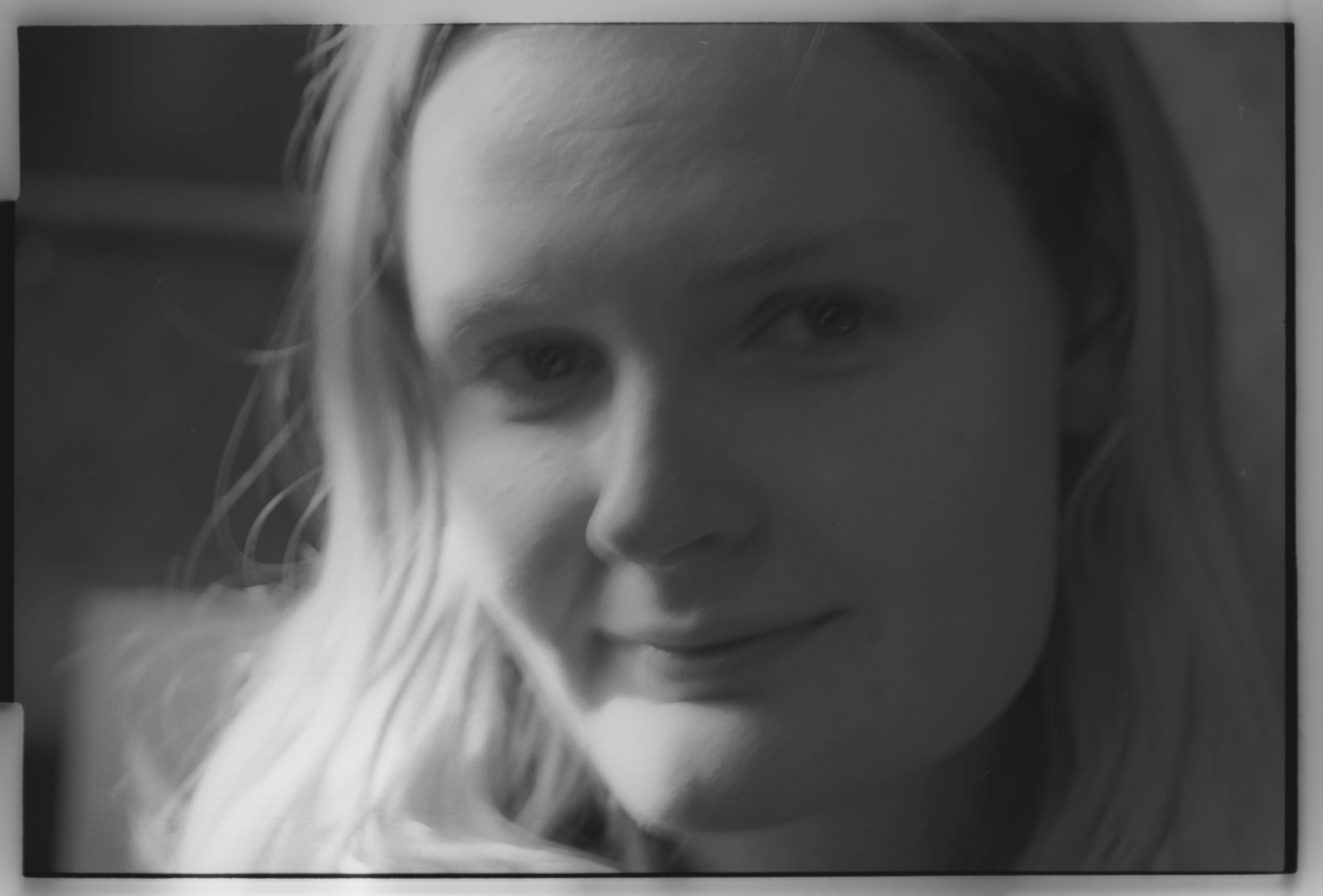 Soft-focus close portrait of Liddy with hair across the side of her face, an inward smile, mono with fine grain.