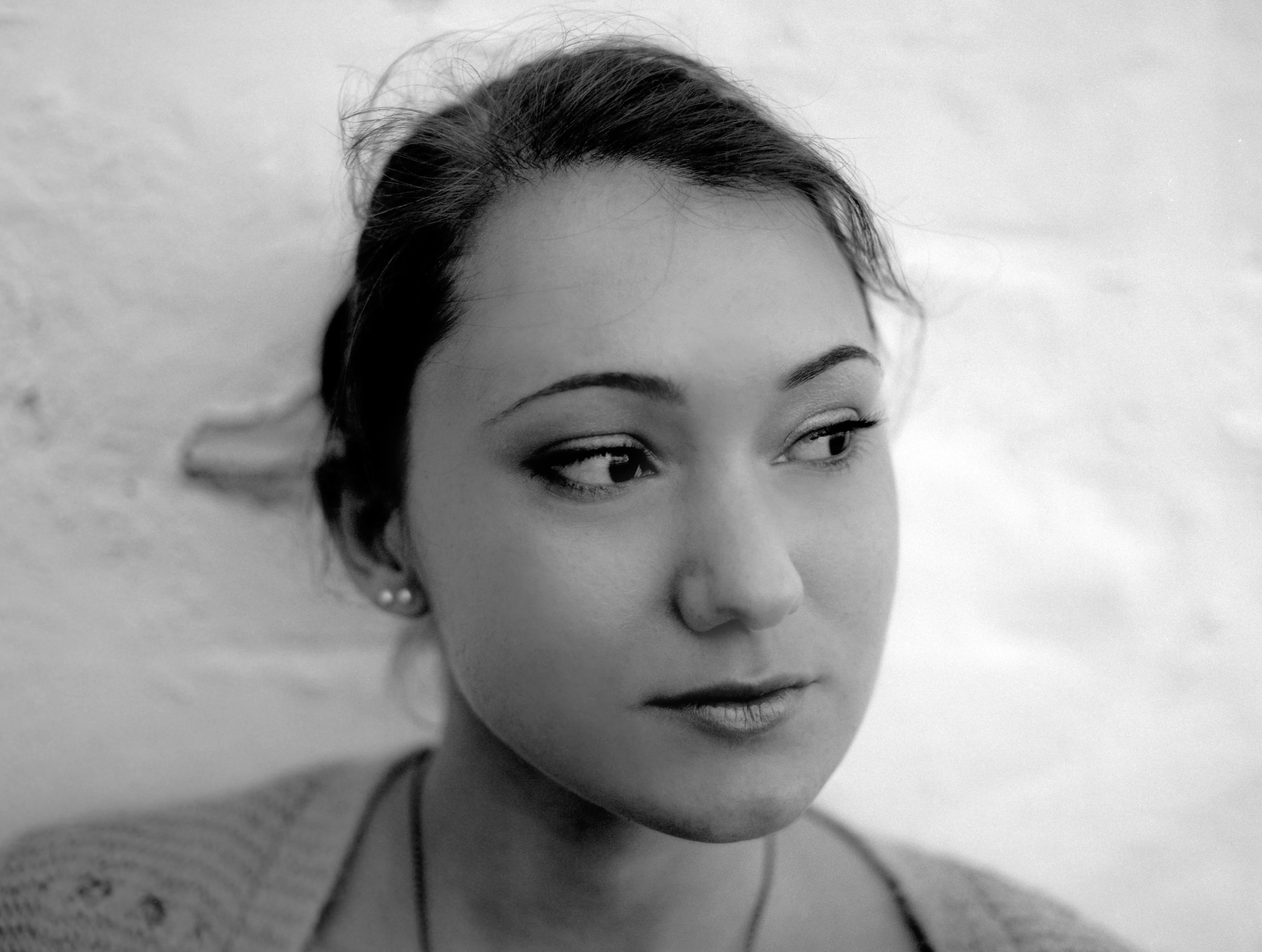 Black-and-white close portrait of a young woman looking off to her right, hair tied back, against a pale wall.