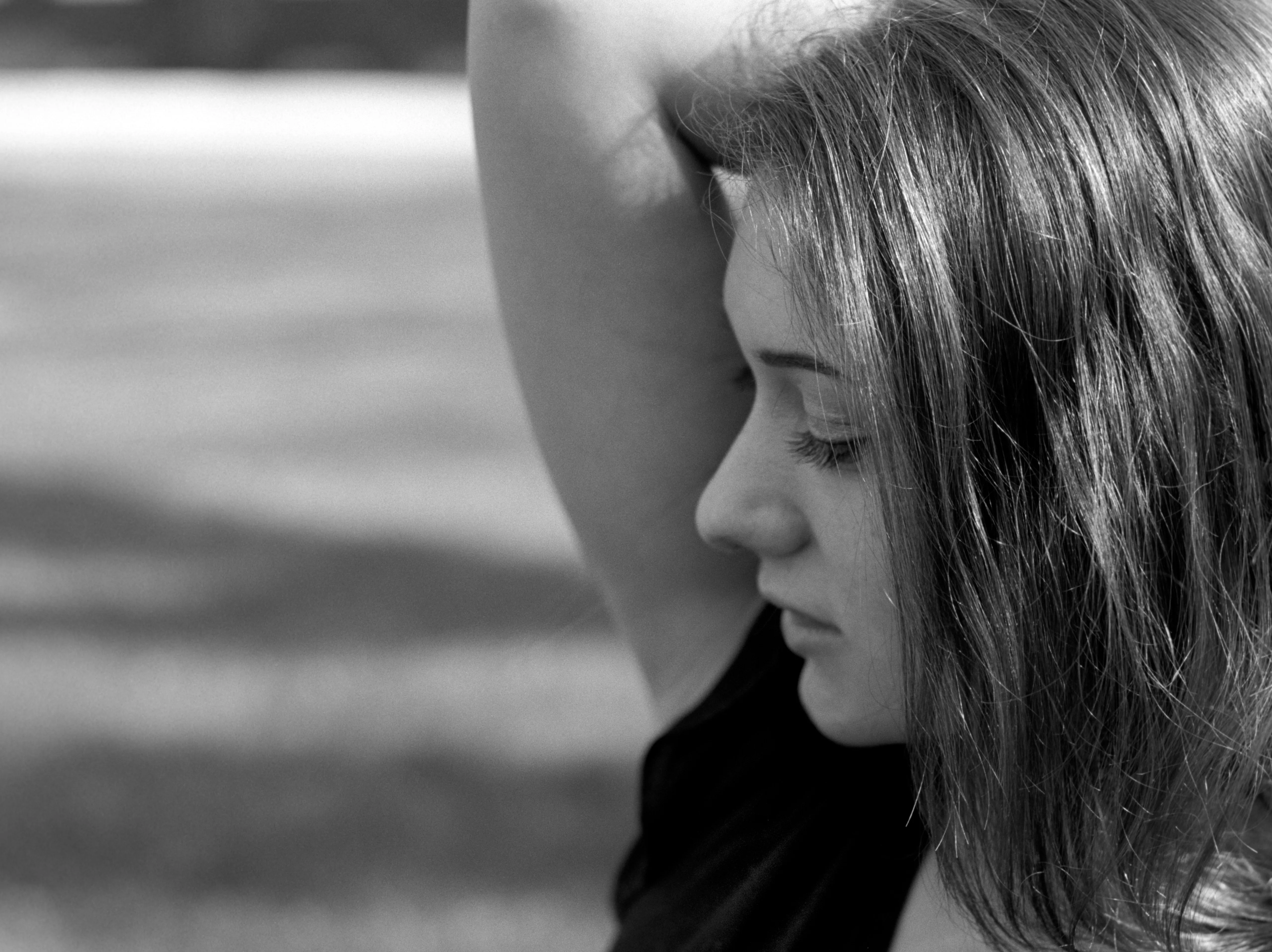 Black-and-white photograph of a young woman in profile, one arm raised to her head, hair falling loose.