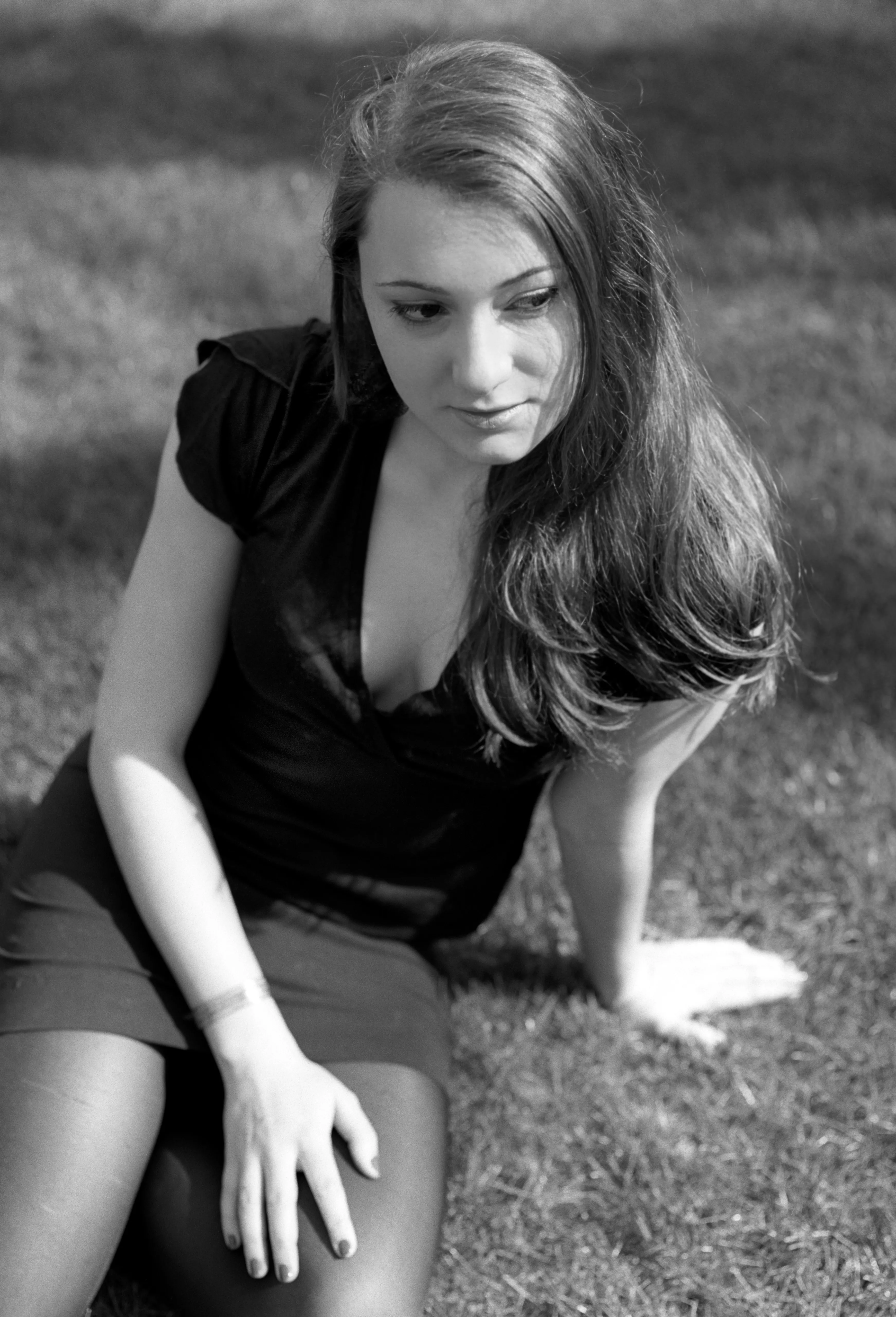 Black-and-white photograph of a young woman in a dark dress sitting on grass, looking down.