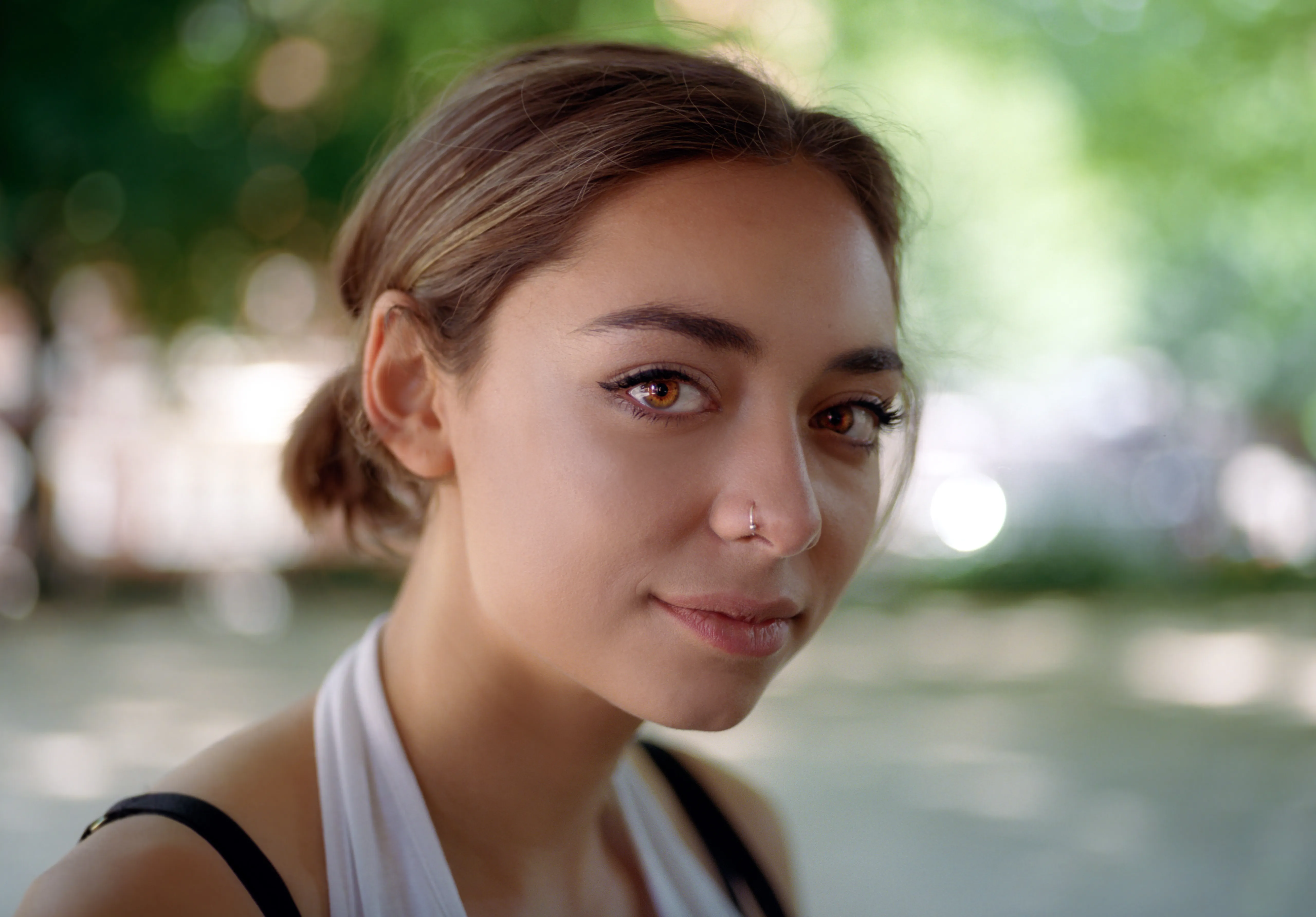 A close portrait of Riya in a park, turned slightly towards the camera with a calm expression, dappled green light behind her.