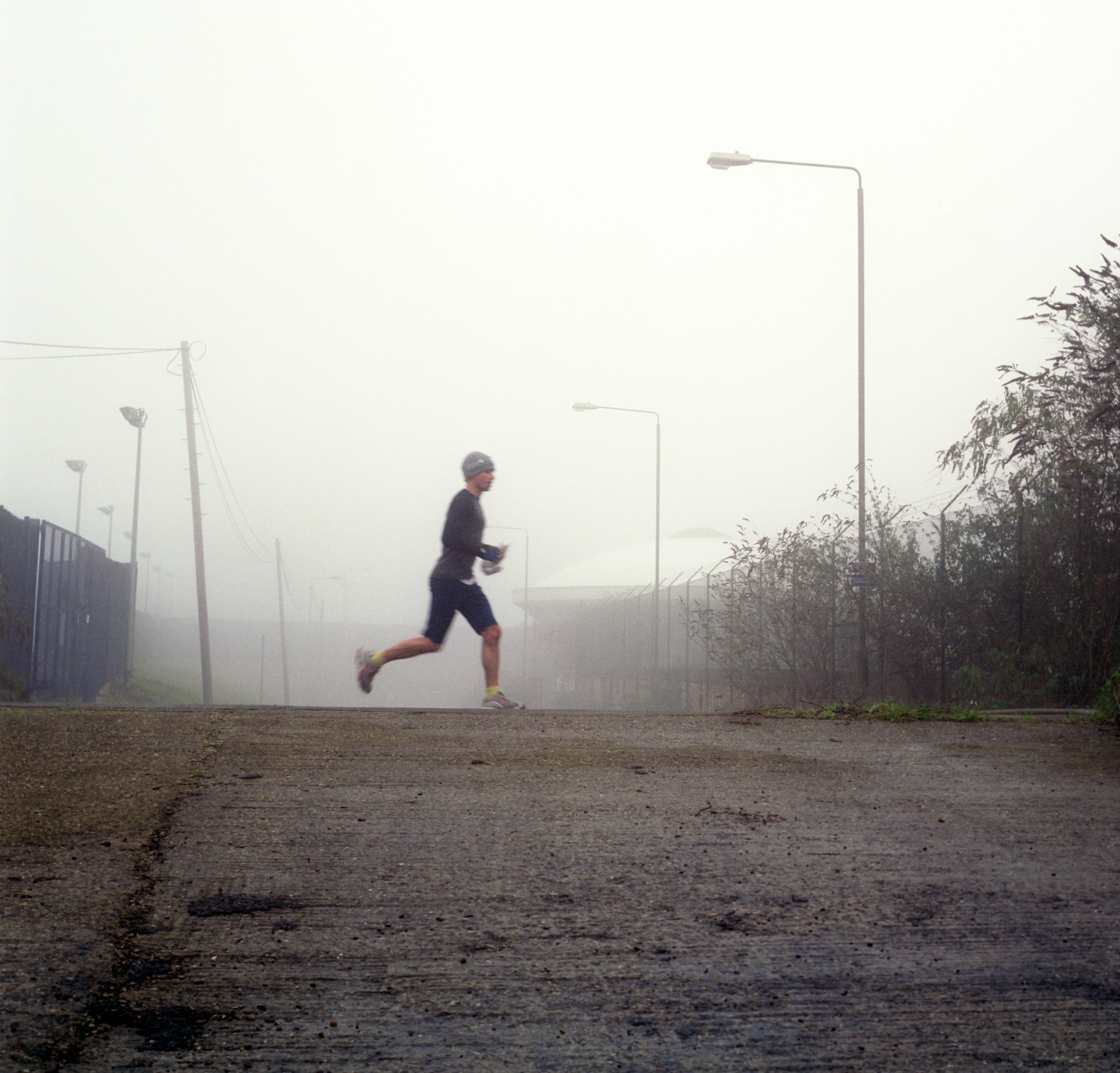 A lone runner mid-stride on an empty fog-bound road, streetlamps fading into the mist behind.