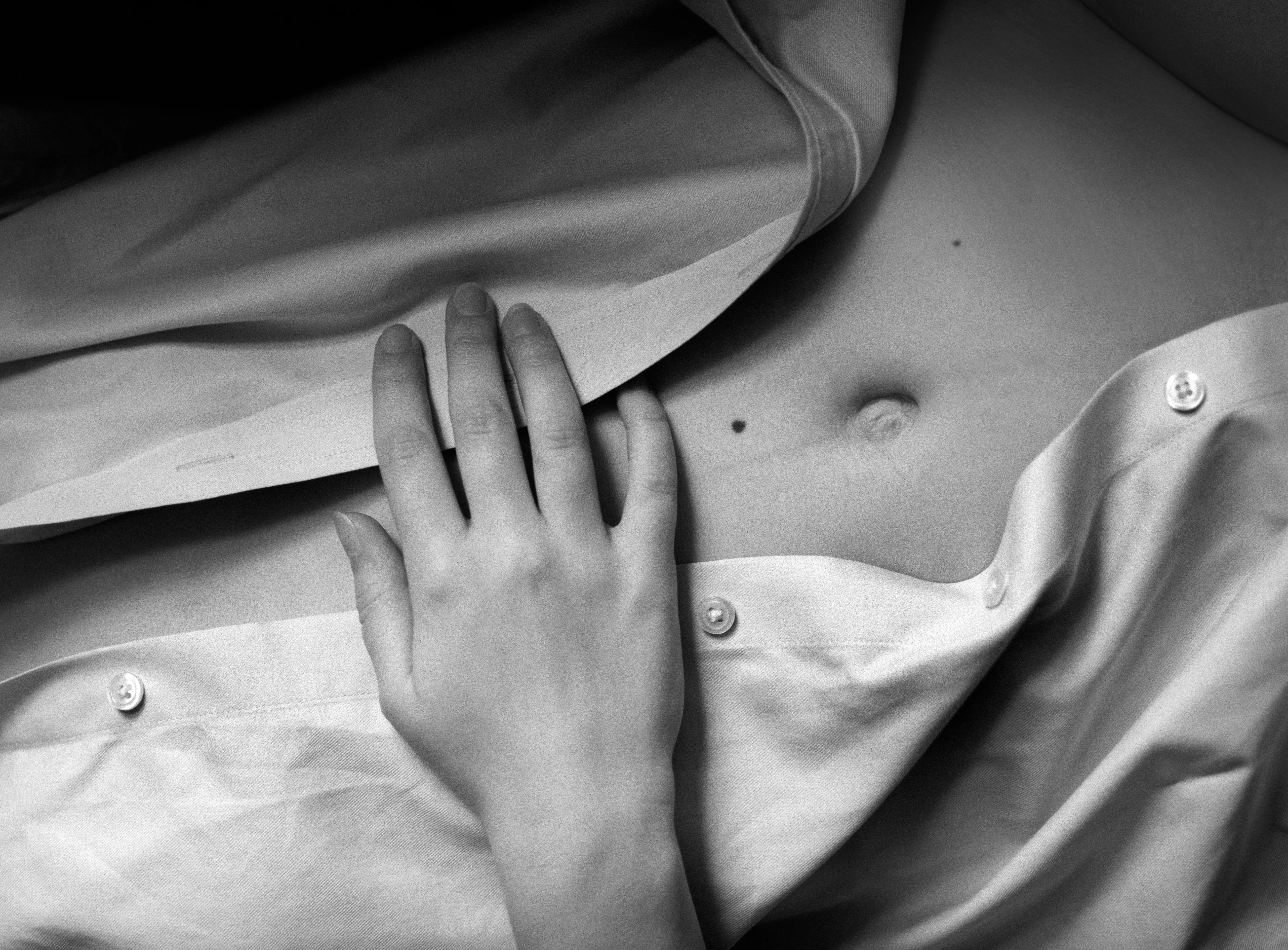 Close still life: a woman's hand rests on a rumpled white shirt with pearl snap-fasteners, part of her torso at the frame edge.