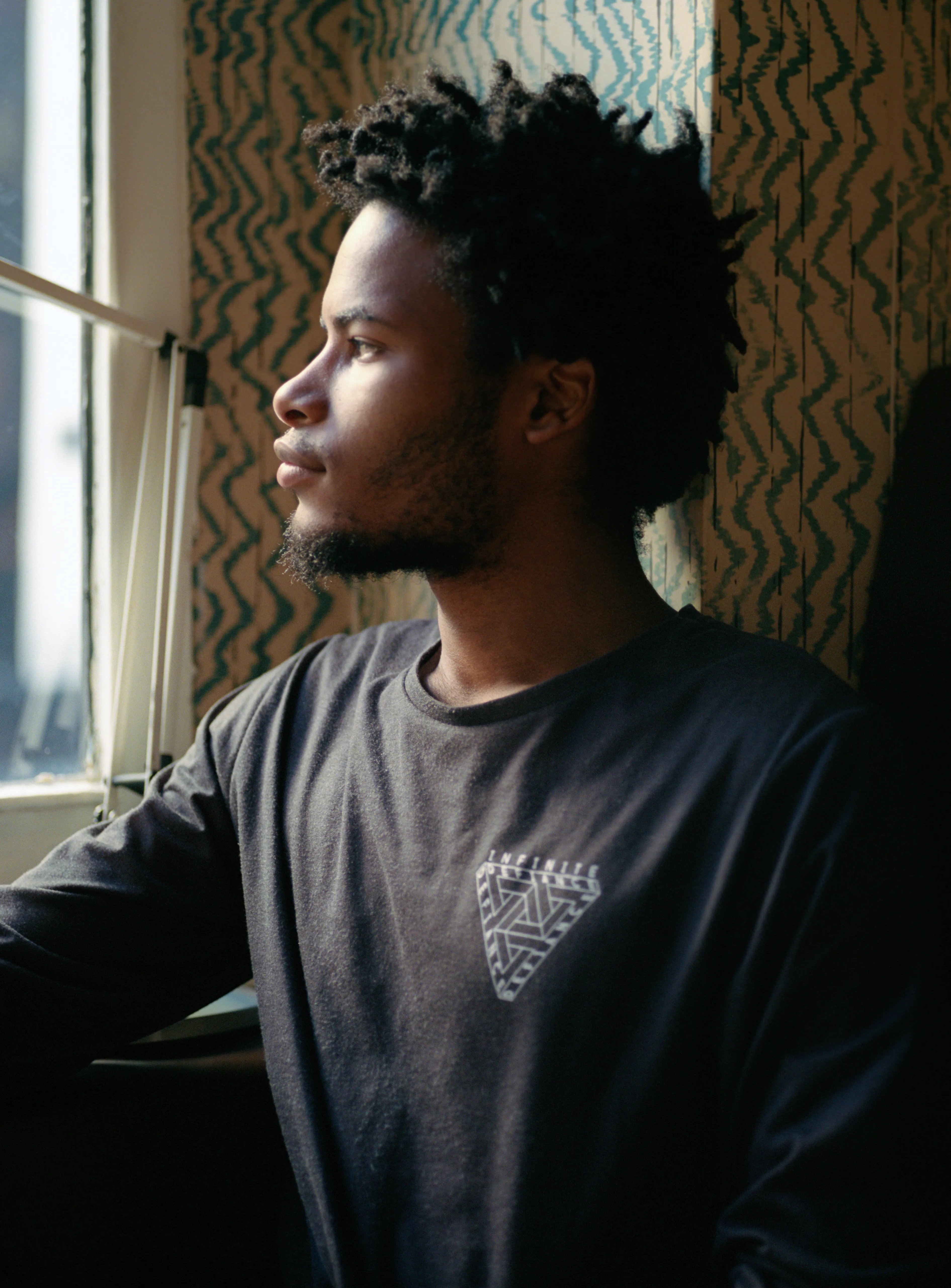 Daniel in profile beside a window, lit from the side, a patterned wall behind him.