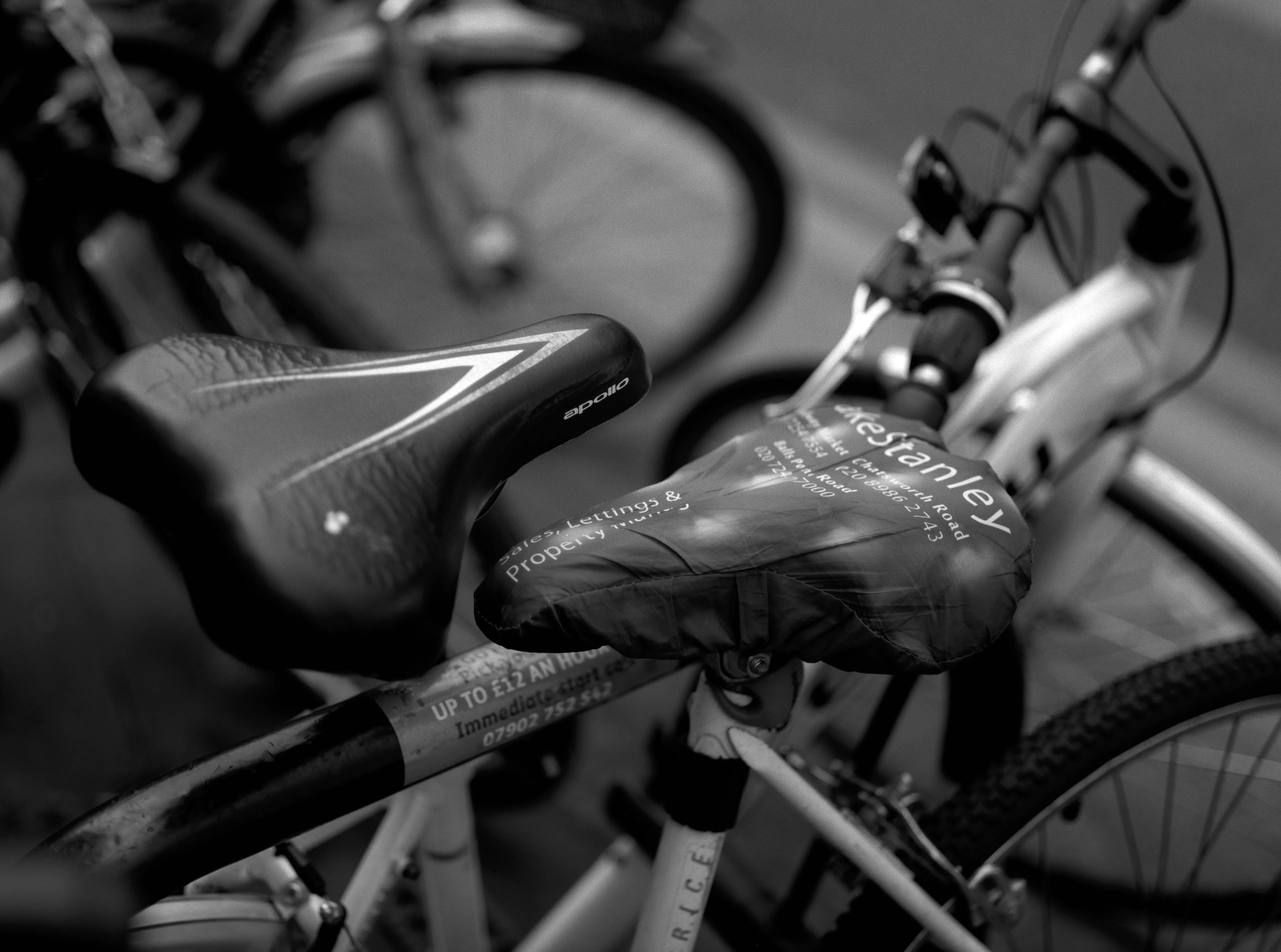 Two bicycles side by side in close-up, one saddle bare, the other under an estate agent's printed cover.