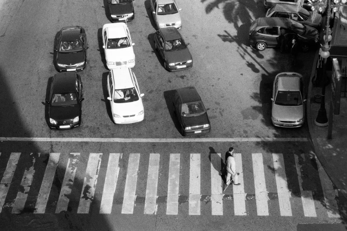 From above — two figures cross on the zebra stripes while ranks of cars stand waiting.