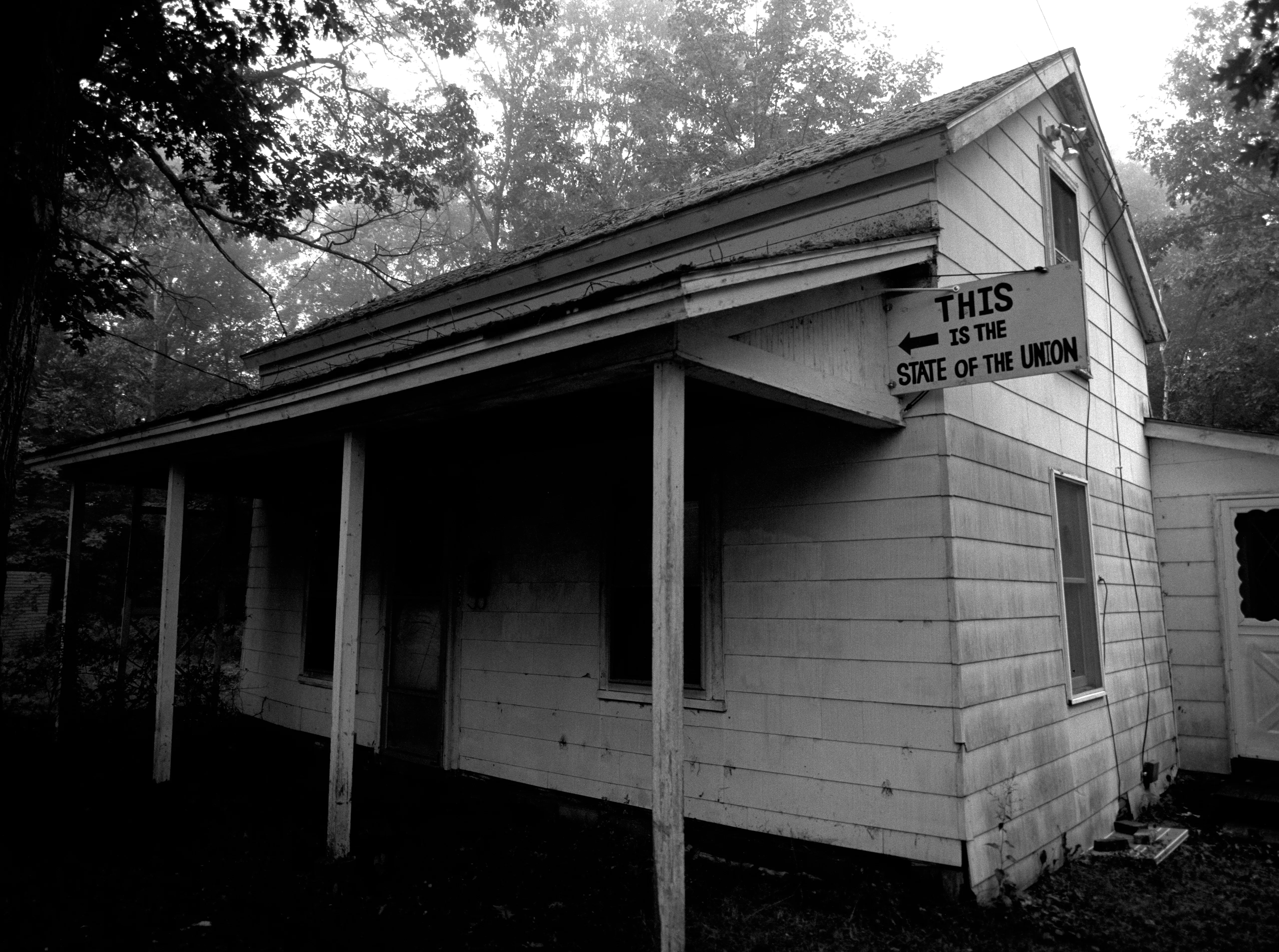 A small clapboard house on Silver Lake Street in dawn fog, a hand-painted sign under the eaves — THIS IS THE STATE OF THE UNION — its arrow pointing back at the house.