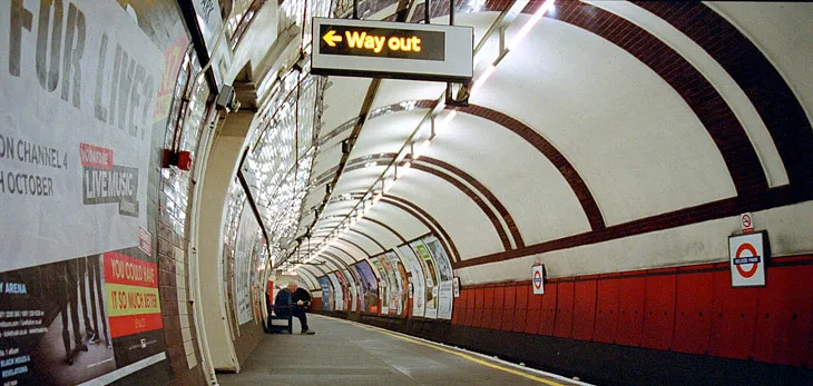 A long London Underground platform, a few passengers strung out along the wait.