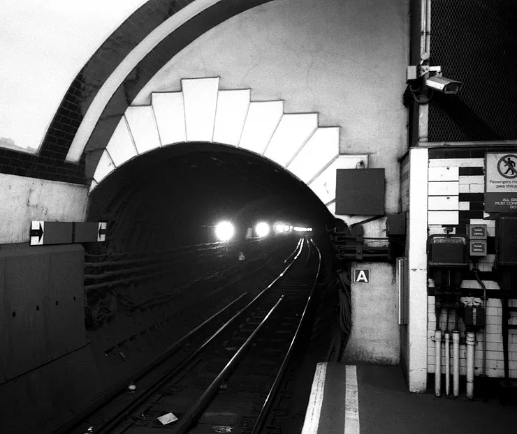 A figure caught in thought on the Underground, gaze fixed on something unseen.