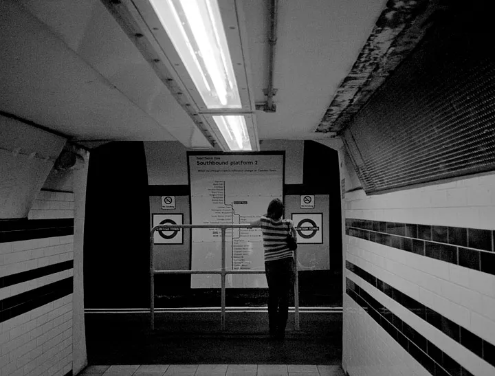Passengers spaced out along a London Underground platform, waiting.