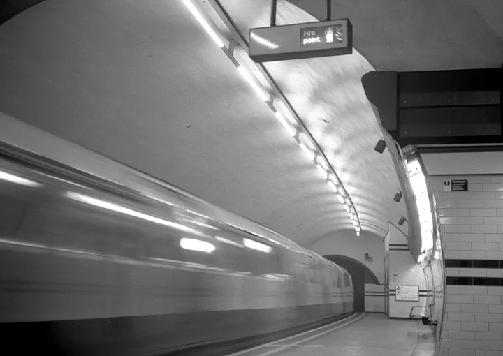 A train rushing through a London Underground station in a blur of motion.