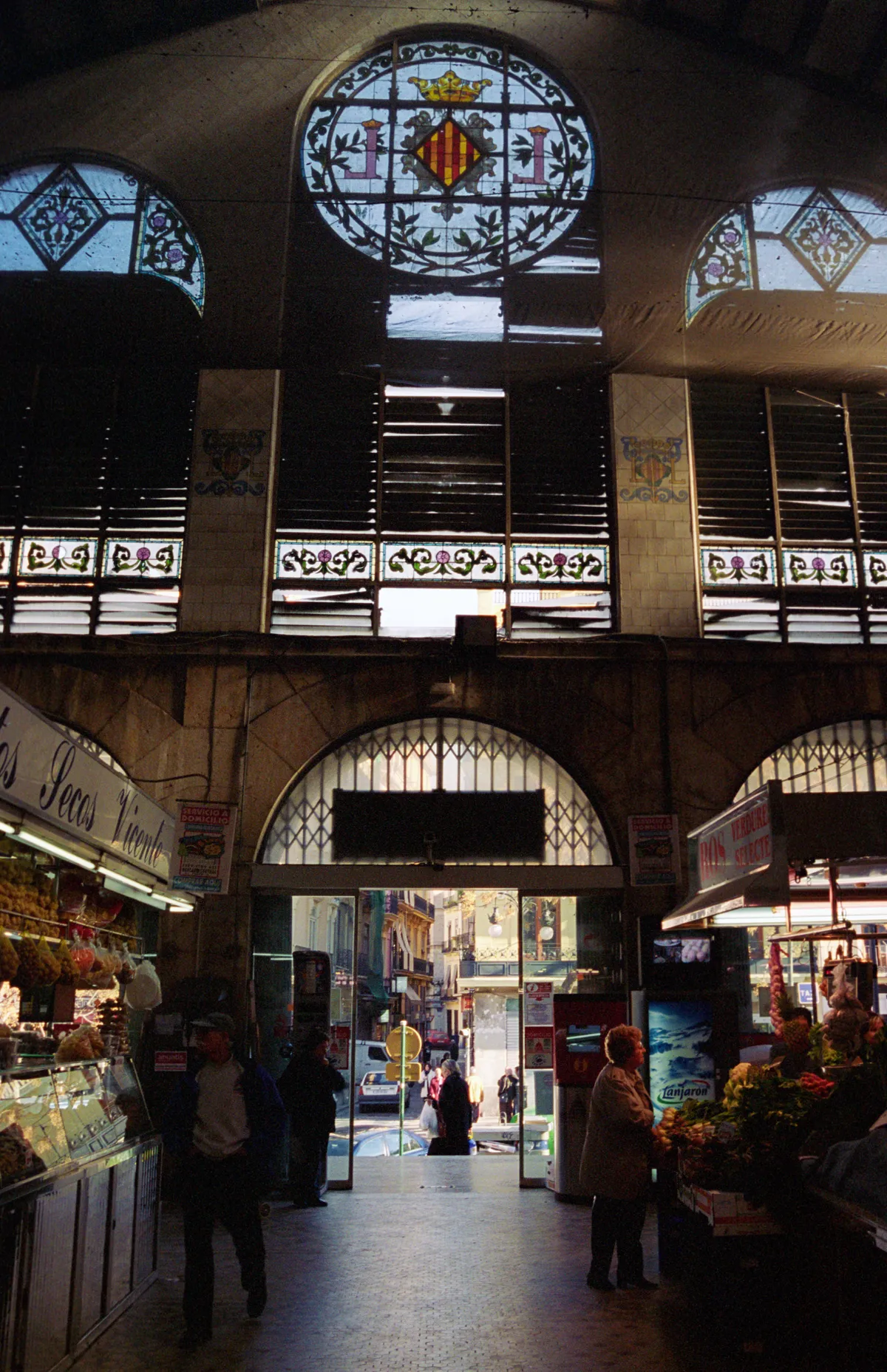 The market entrance from inside — stained glass and louvres above, the sunlit street framed in the open door.